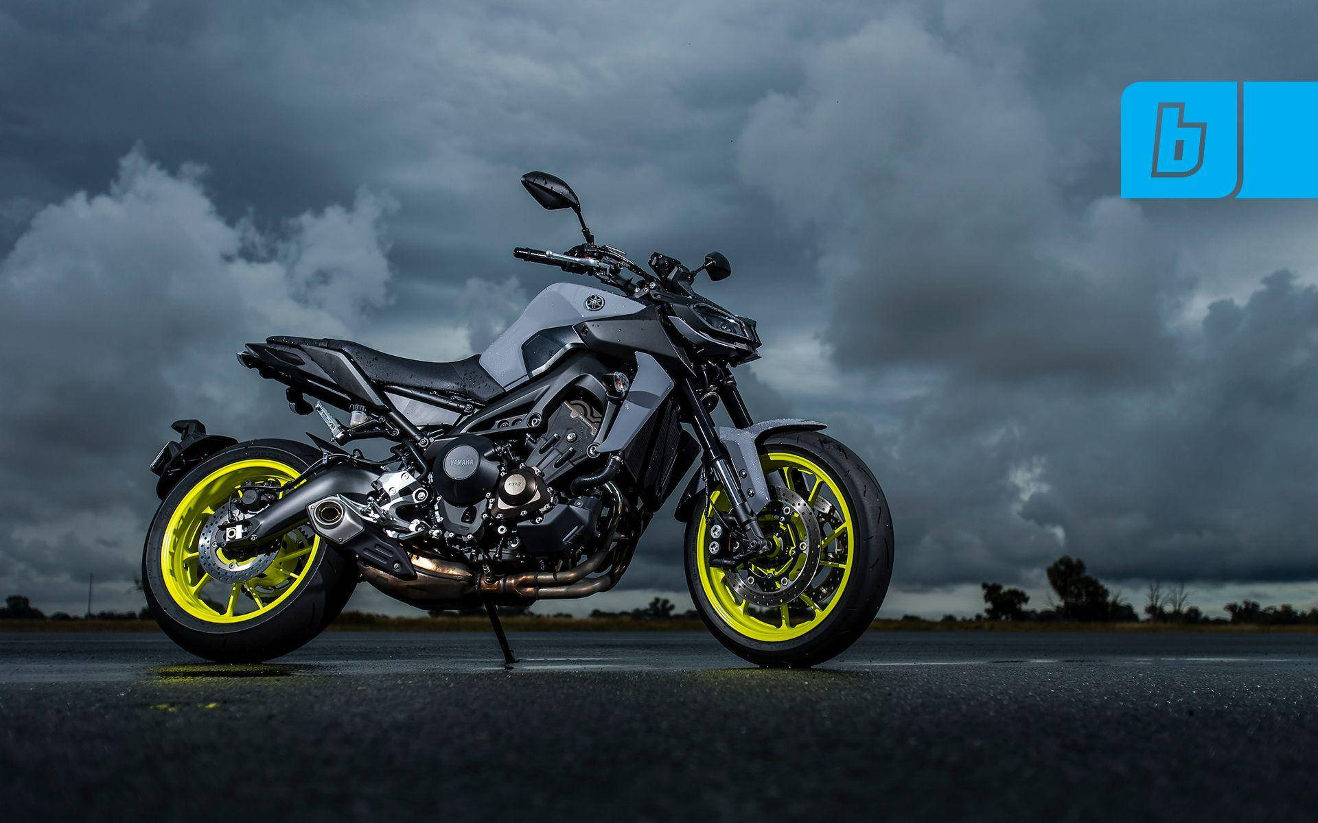 yamaha mt 15 桌布 壁紙 — 一台時尚的灰色機車配備螢光黃色車輪，在戲劇性的暴風雨天空下，佇立在潮濕的瀝青路面上。