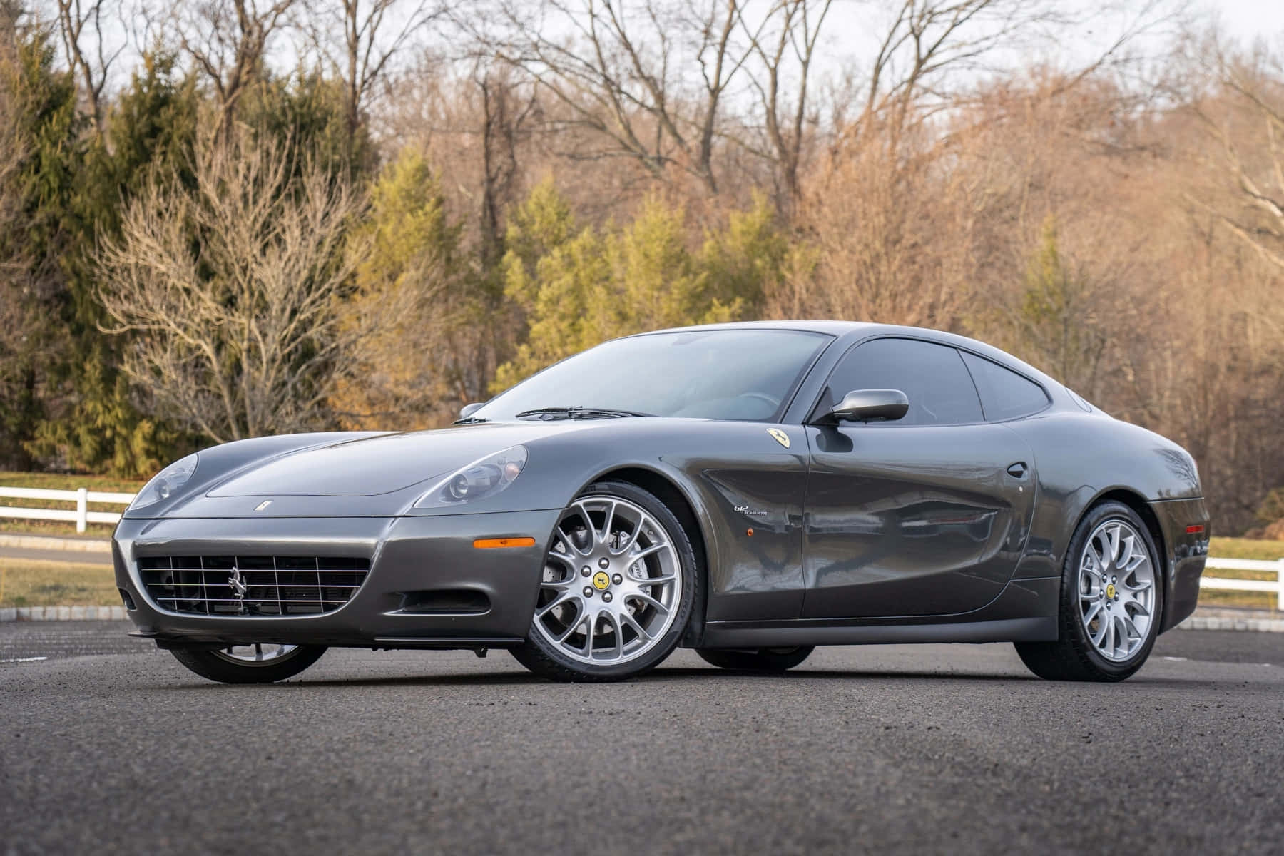Ferrari 612 Scaglietti 桌布 壁紙 — 一台時尚的灰色法拉利612 Superamerica停在柏油路上，背景有光禿禿的樹木和常綠植物。