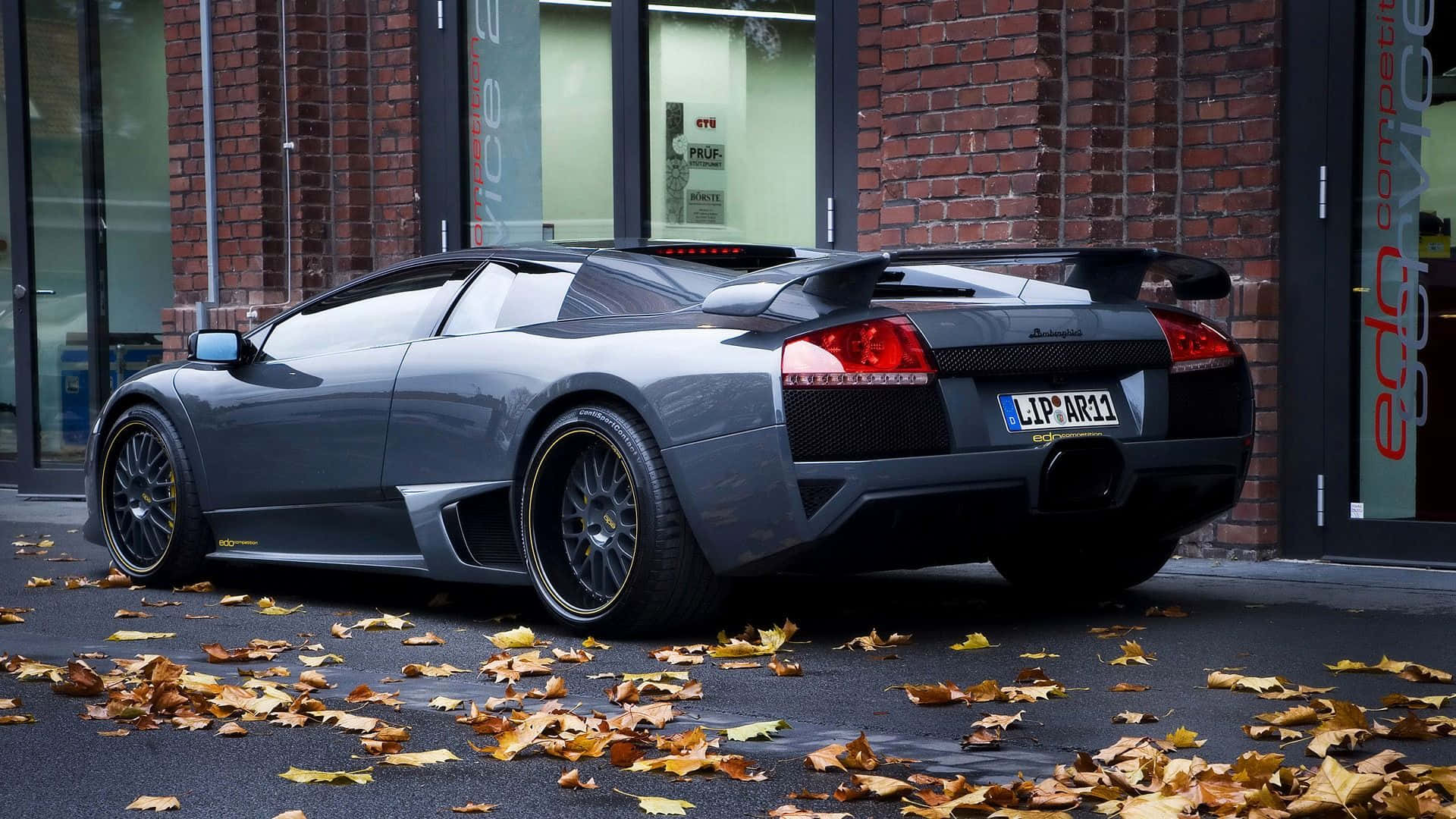 Cool Lamborghini 桌布 壁紙 — 一台時尚的灰色藍寶堅尼Murciélago LP640停泊在濕漉漉的街道上，散落著秋天的落葉，背景是磚砌建築。