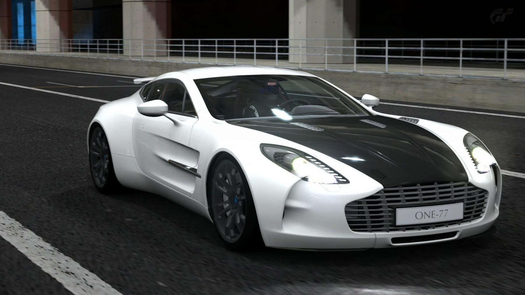Aston Martin One-77 桌布 壁紙 — 一台時尚的白色 Aston Martin One-77，帶有黑色引擎蓋條紋，在人造燈光下於黑暗賽道上疾馳。