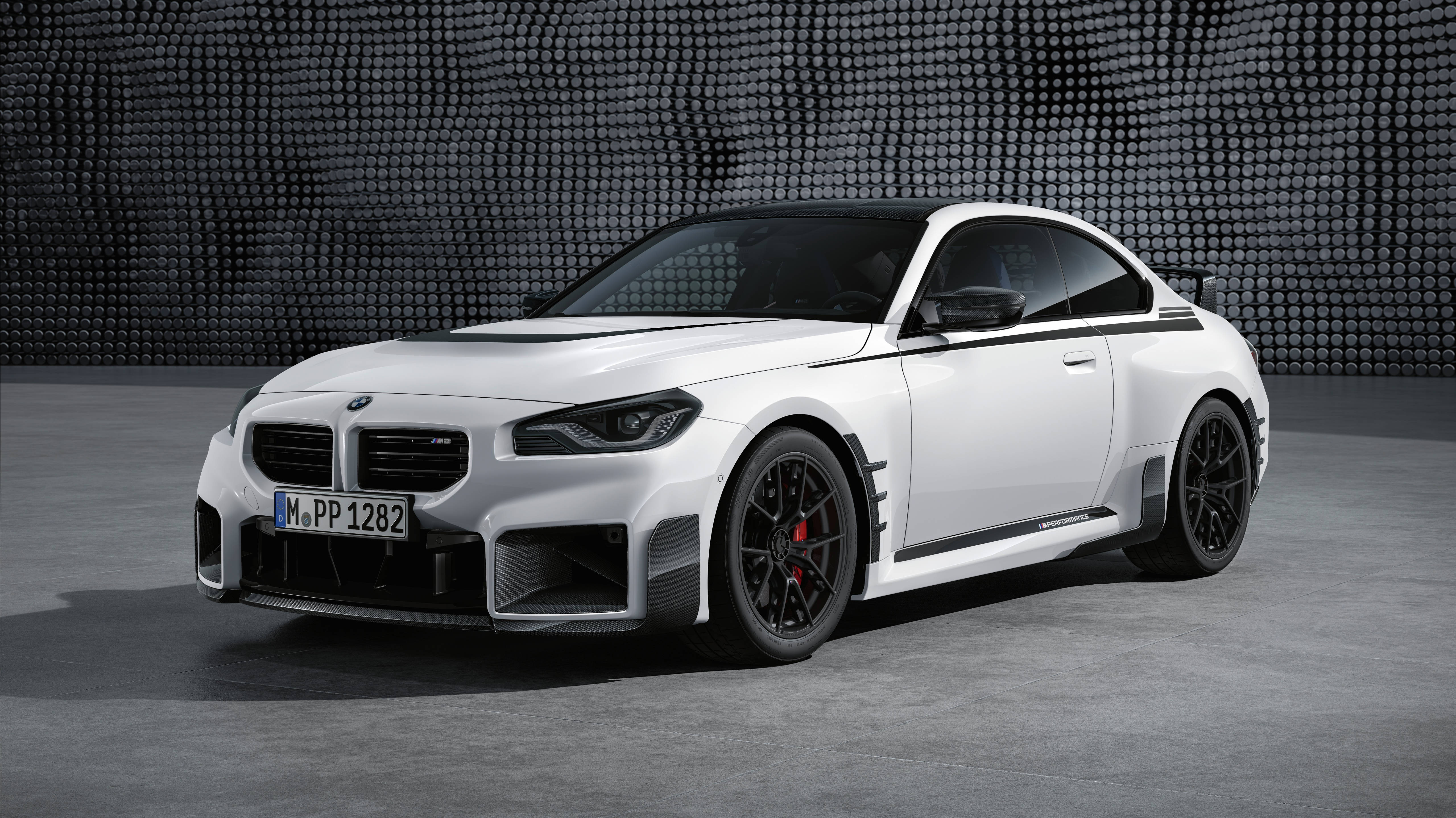 Bmw Cars 桌布 壁紙 — 一台時尚的白色BMW M2 Competition雙門轎跑車，帶有黑色飾件和紅色制動卡鉗，在簡約的攝影棚環境中，對著有紋理的灰色牆壁蓄勢待發。