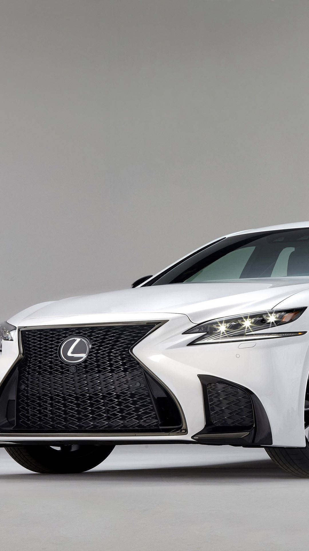 lexus iPhone 桌布 壁紙 — 一台時尚的白色Lexus轎車在簡約灰色工作室背景下展示其大膽的格柵和銳利的LED頭燈。