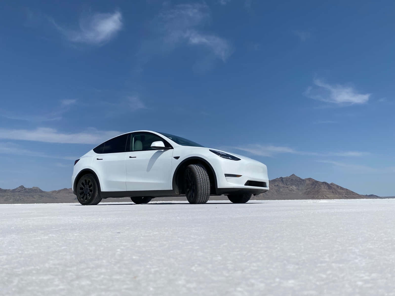 特斯拉 桌布 壁紙 — 一台時尚的白色Tesla Model Y獨自停放在廣闊的鹽灘上，背景是晴朗的藍天和遠山。