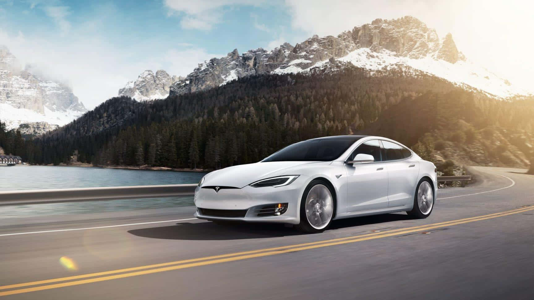 Tesla Model 3 桌布 壁紙 — 一台時尚的白色Tesla Model S沿著蜿蜒的道路行駛，旁邊是平靜的湖泊，背景是白雪覆蓋的山脈。