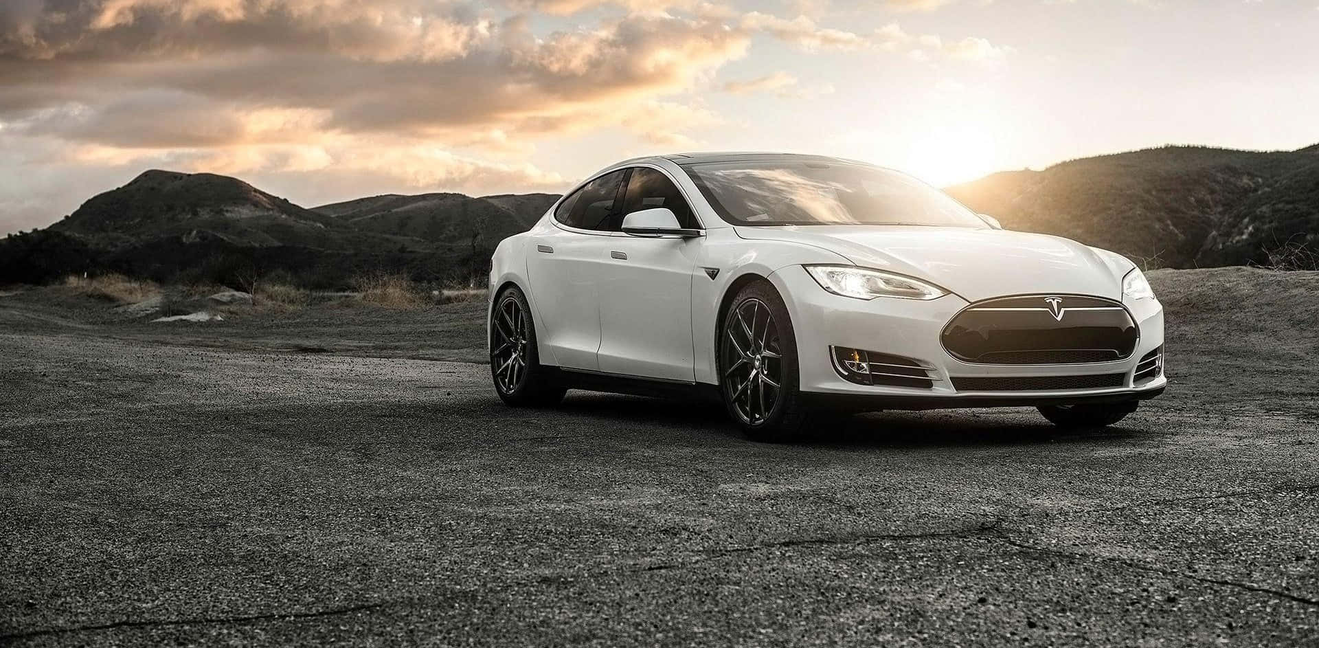 Hybrid Car 桌布 壁紙 — 一台時尚的白色Tesla Model S停在裂開的柏油路上，背後是起伏的丘陵和金色的夕陽。