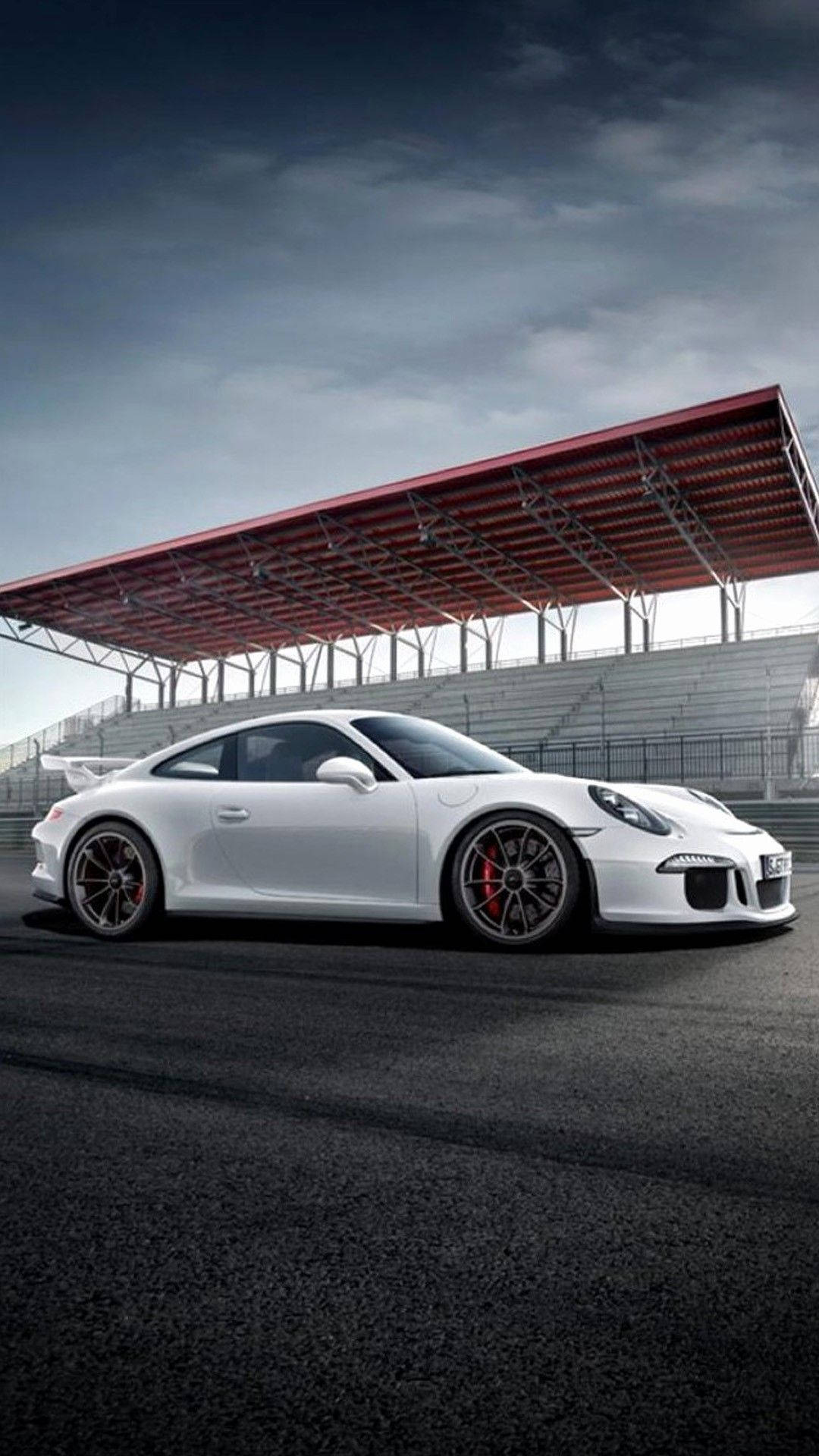 X 桌布 壁紙 — 一台時尚的白色保時捷911 GT3 RS跑車停泊在賽道上，背景是戲劇性的多雲天空和紅色頂篷看台。