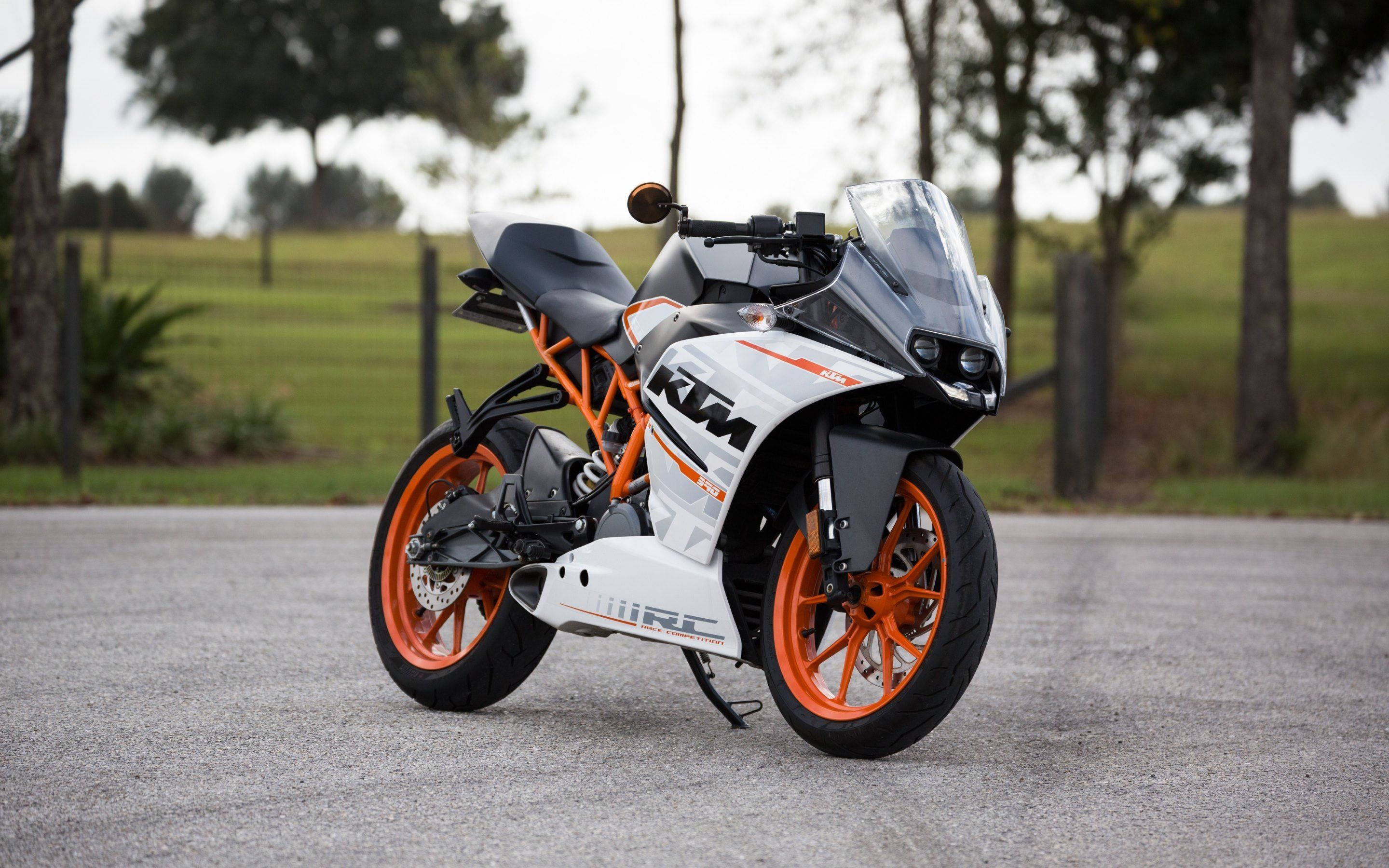 Ktm Bike 桌布 壁紙 — 一台時尚的白色和橙色KTM RC機車停在柏油路上，背景有樹木和草地。