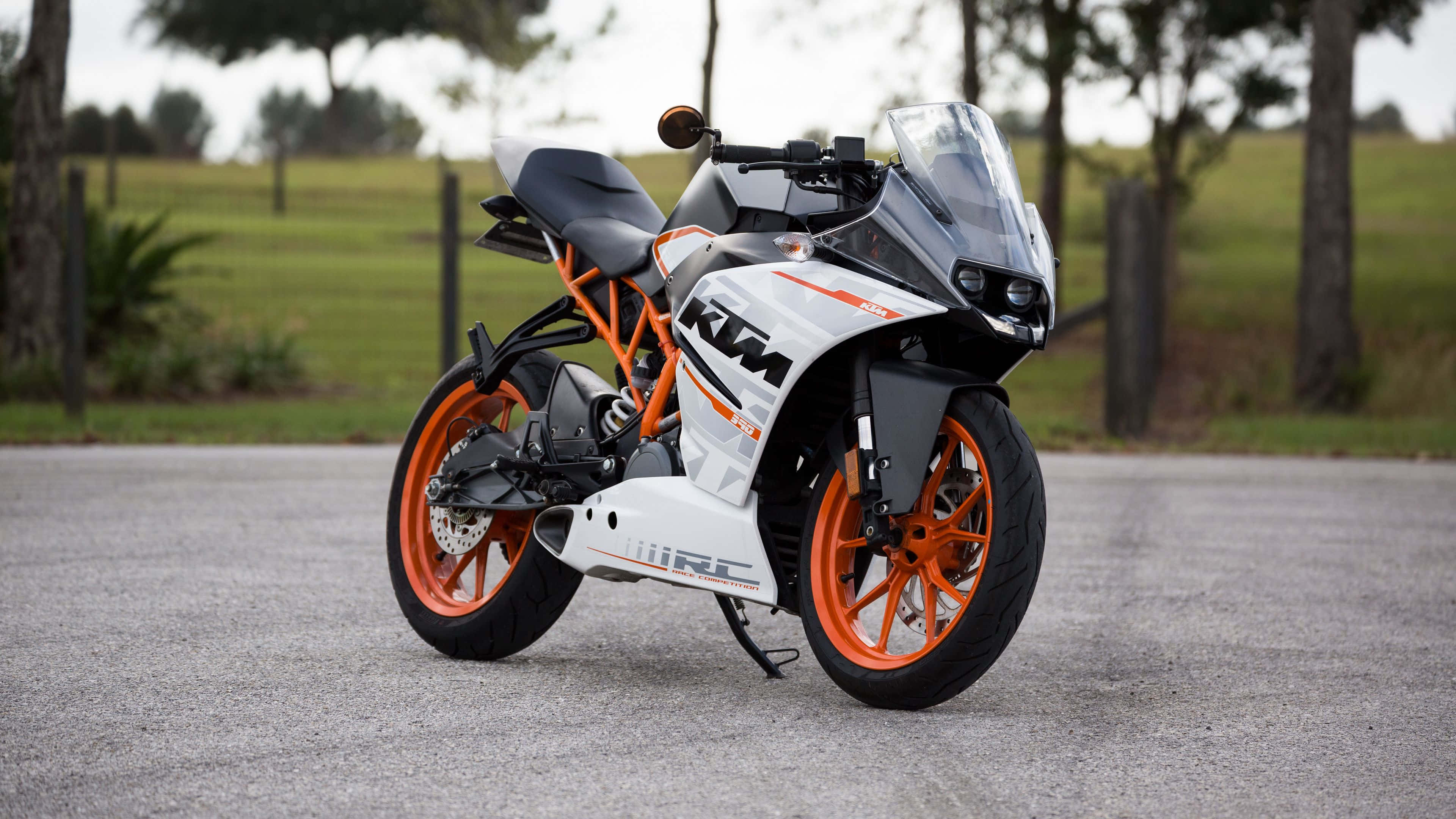 桌布 壁紙 — 一台時尚的白色和橙色KTM RC機車停在碎石路上，背景有樹木和草地。