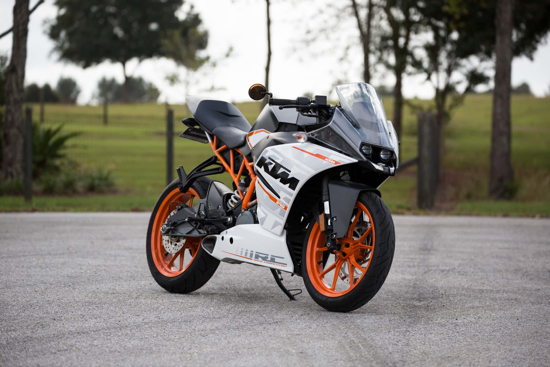 Superbike 桌布 壁紙 — 一台時尚的白色和橙色KTM RC機車停放在碎石路上，背景有樹木和草地。