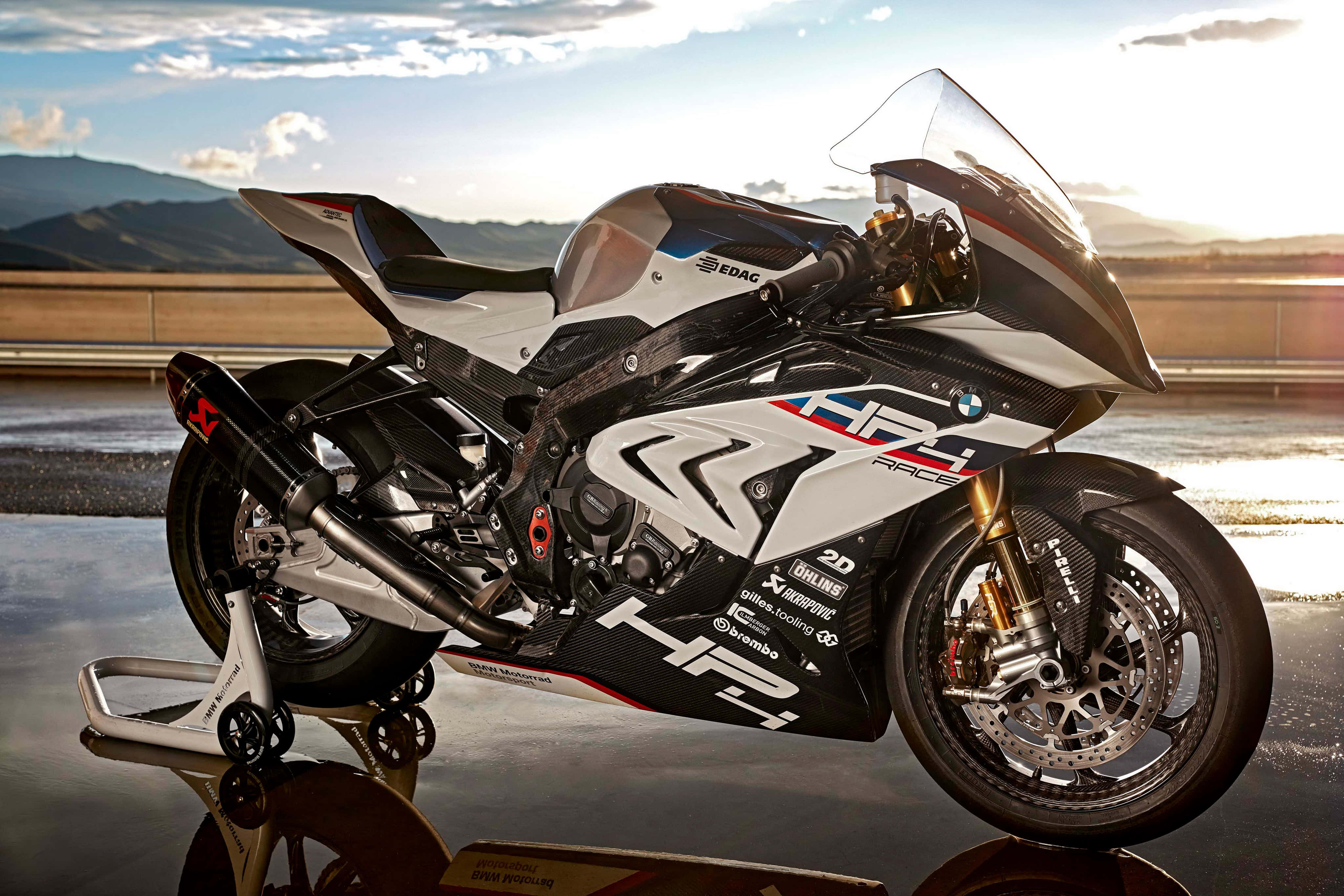 Superbike 桌布 壁紙 — 一台時尚的白色和黑色BMW HP4 Race摩托車在金色日落光線下，在反射的濕路上閃耀，背景是山脈。