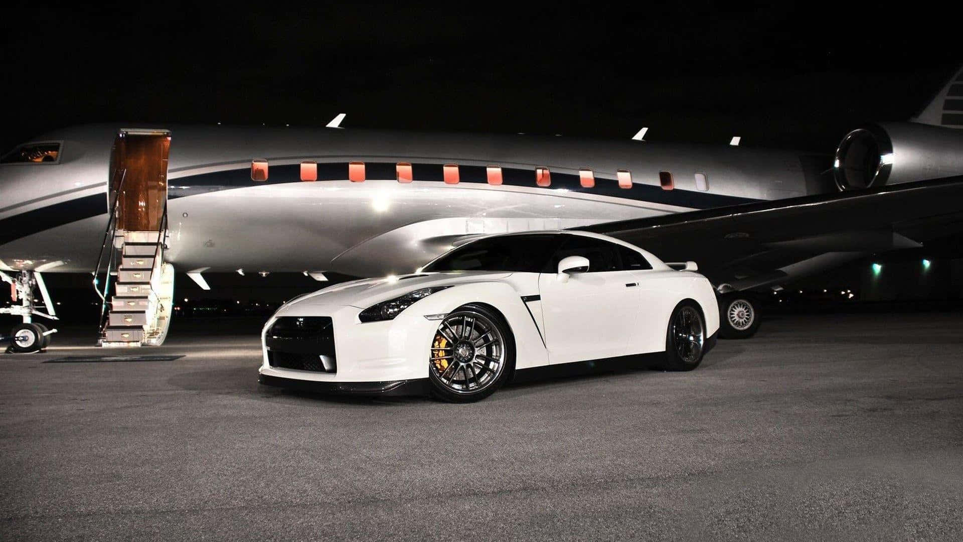 飛機 桌布 壁紙 — 一台時尚的白色日產GT-R在夜間停泊在瀝青停機坪上，旁邊是一架樓梯已放下的私人飛機。