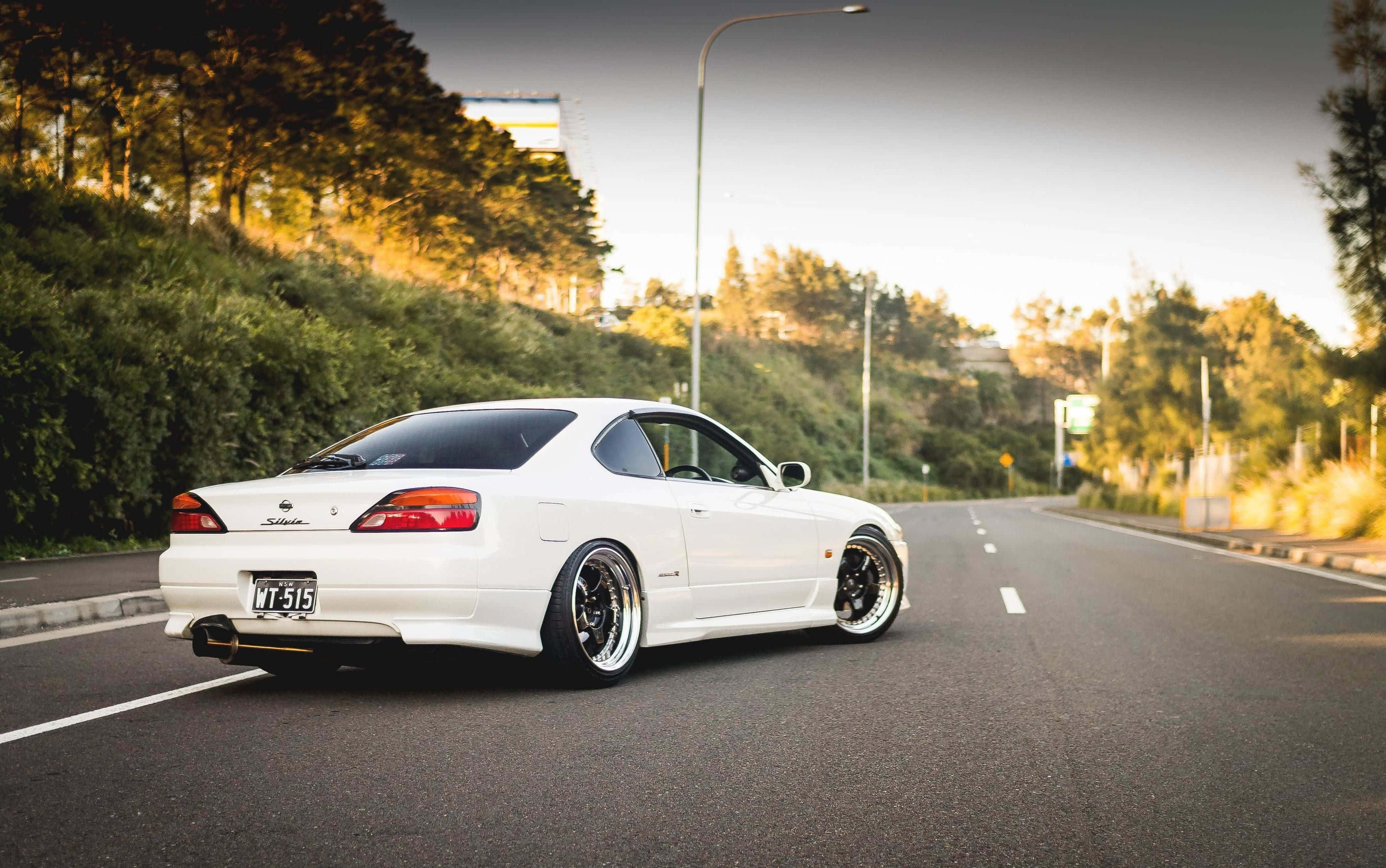 Nissan Silvia S15 桌布 壁紙 — 一台時尚的白色日產Silvia S15跑車配備訂製輪圈，在黃金時段沿著綠樹成蔭的道路行駛。