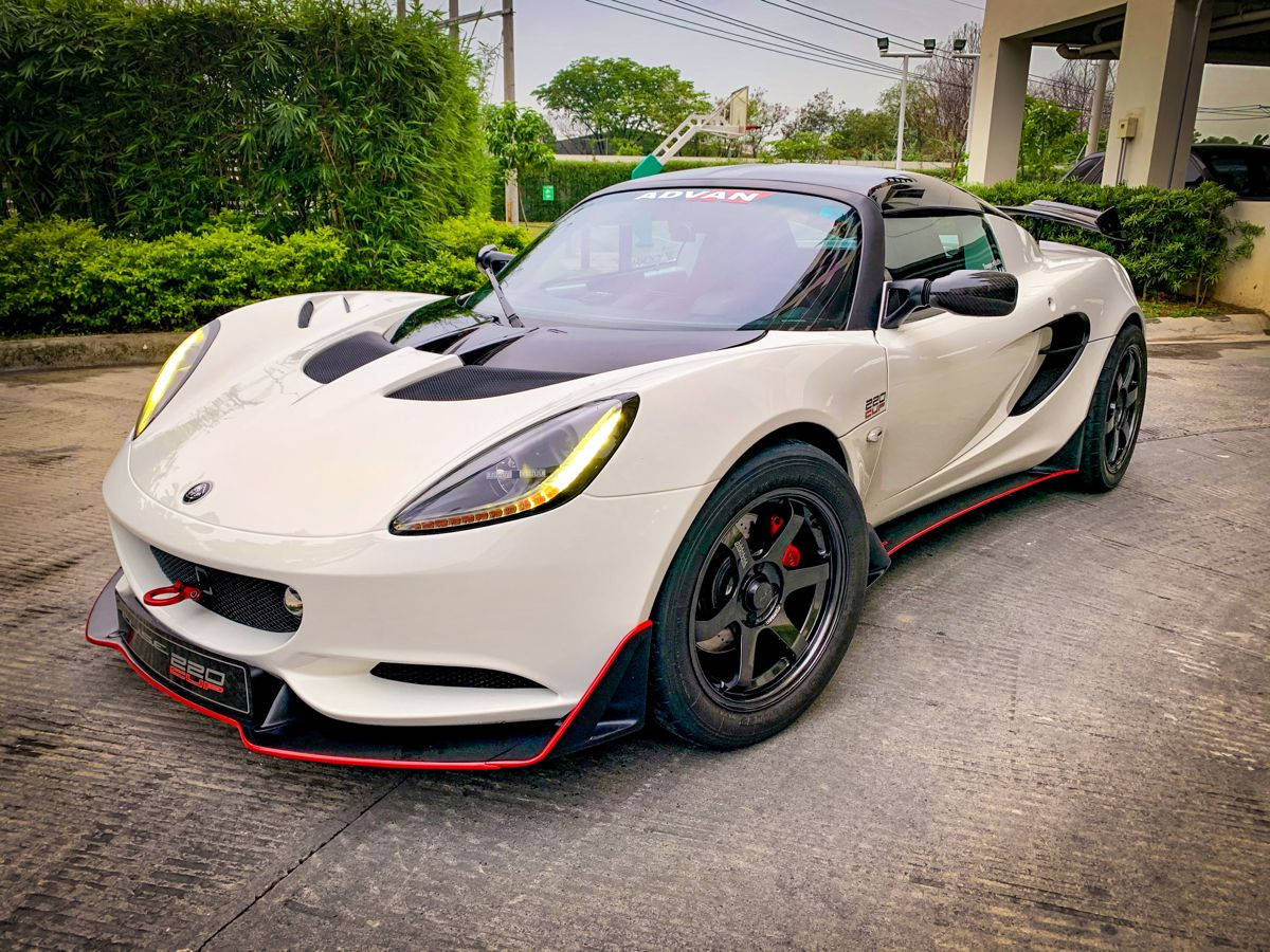 跑車 桌布 壁紙 — 一台時尚的白色蓮花Exige跑車，帶有紅色點綴，停泊在混凝土停車場，周圍環繞著綠植。