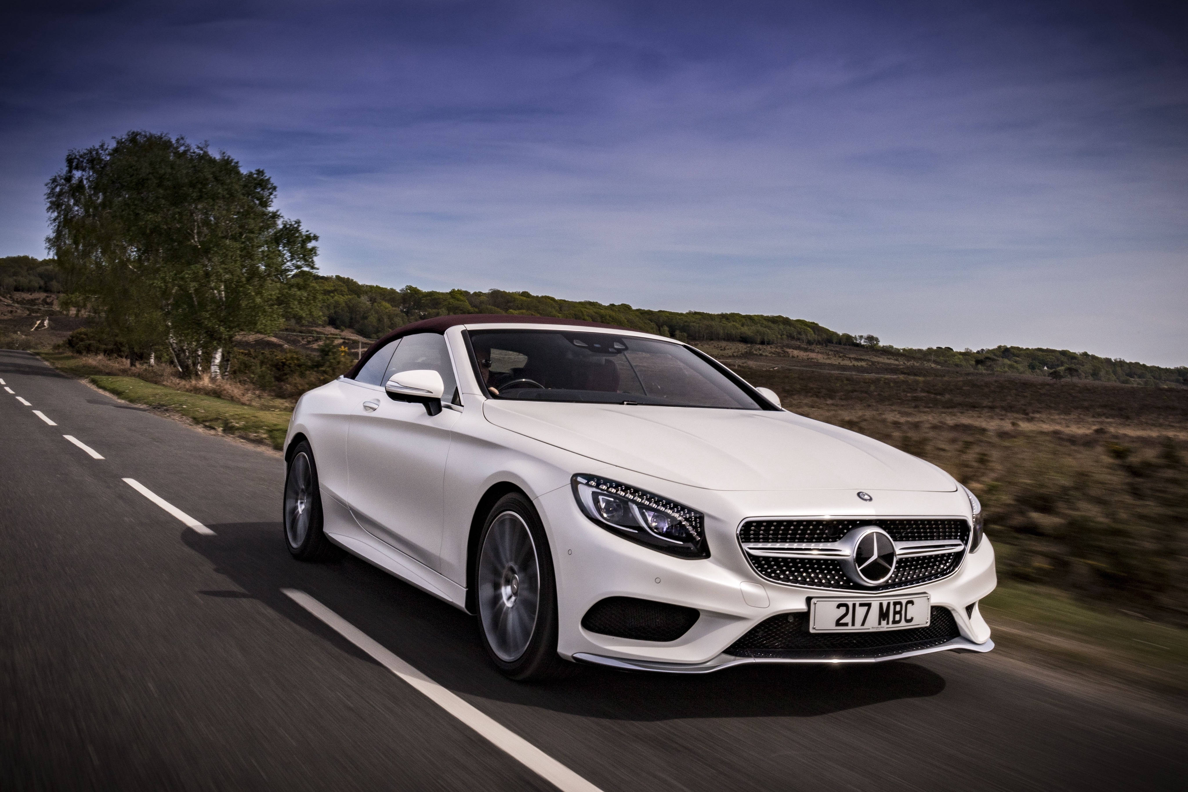 benz 4K 桌布 壁紙 — 一台時尚的白色賓士S-Class敞篷車在晴朗的藍天下沿著蜿蜒的鄉村道路奔馳。
