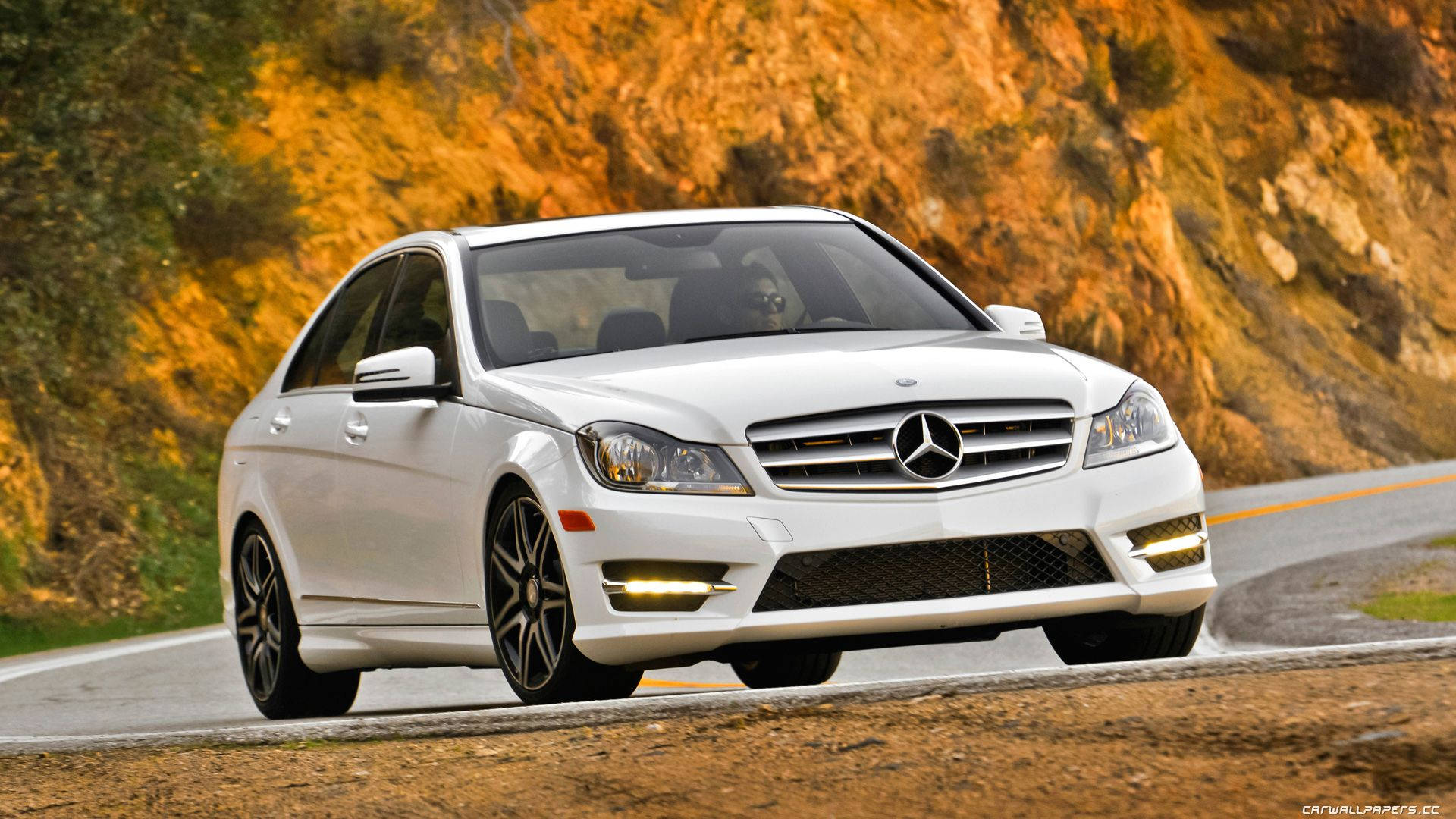 Mercedes Benz C300 桌布 壁紙 — 一台時尚的白色賓士轎車沿著蜿蜒的山路行駛，背景是金棕色的懸崖。