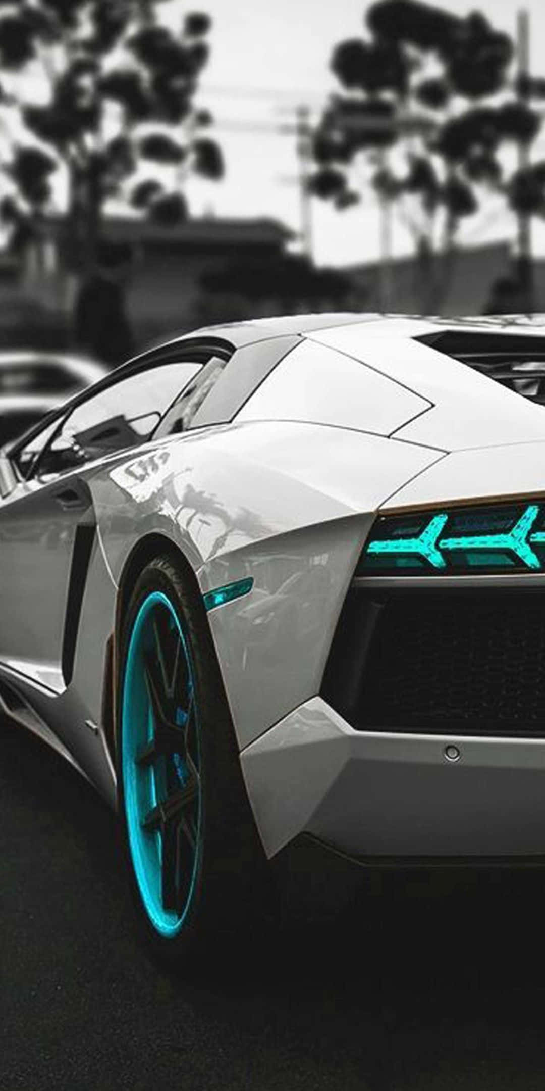 Pixel 3 Lamborghini 桌布 壁紙 — 一台時尚的白色跑車，帶有發光的青色頭燈和輪圈燈，停在背景有模糊樹木的街道上。