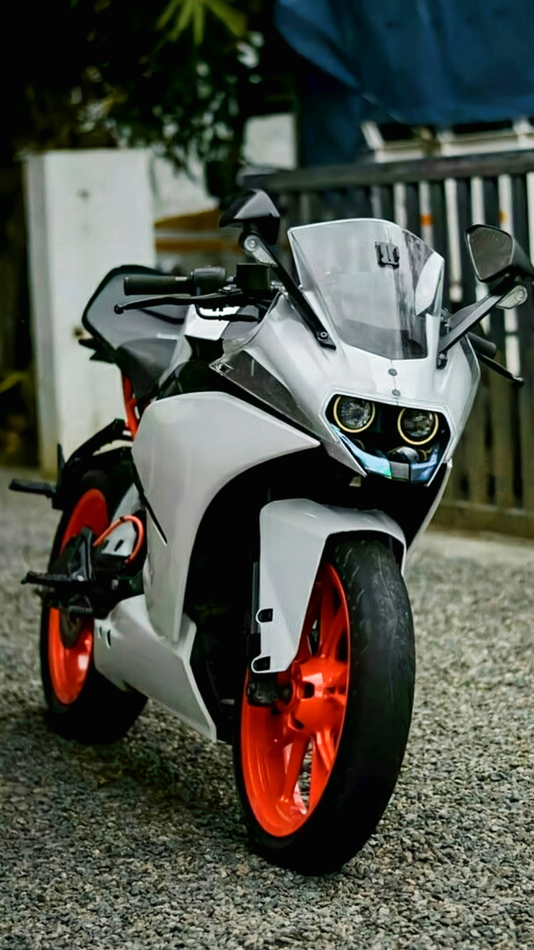 KTM RC 200 桌布 壁紙 — 一台時尚的白色運動機車，配以鮮豔橙色輪胎，停泊在圍欄附近的碎石地上。