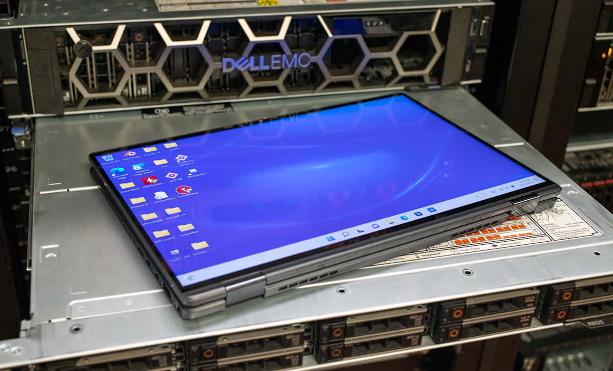 Dell 桌布 壁紙 — 一台時尚的筆記型電腦，帶有藍色Windows桌面，打開放在數據中心的銀色Dell EMC伺服器機架上。