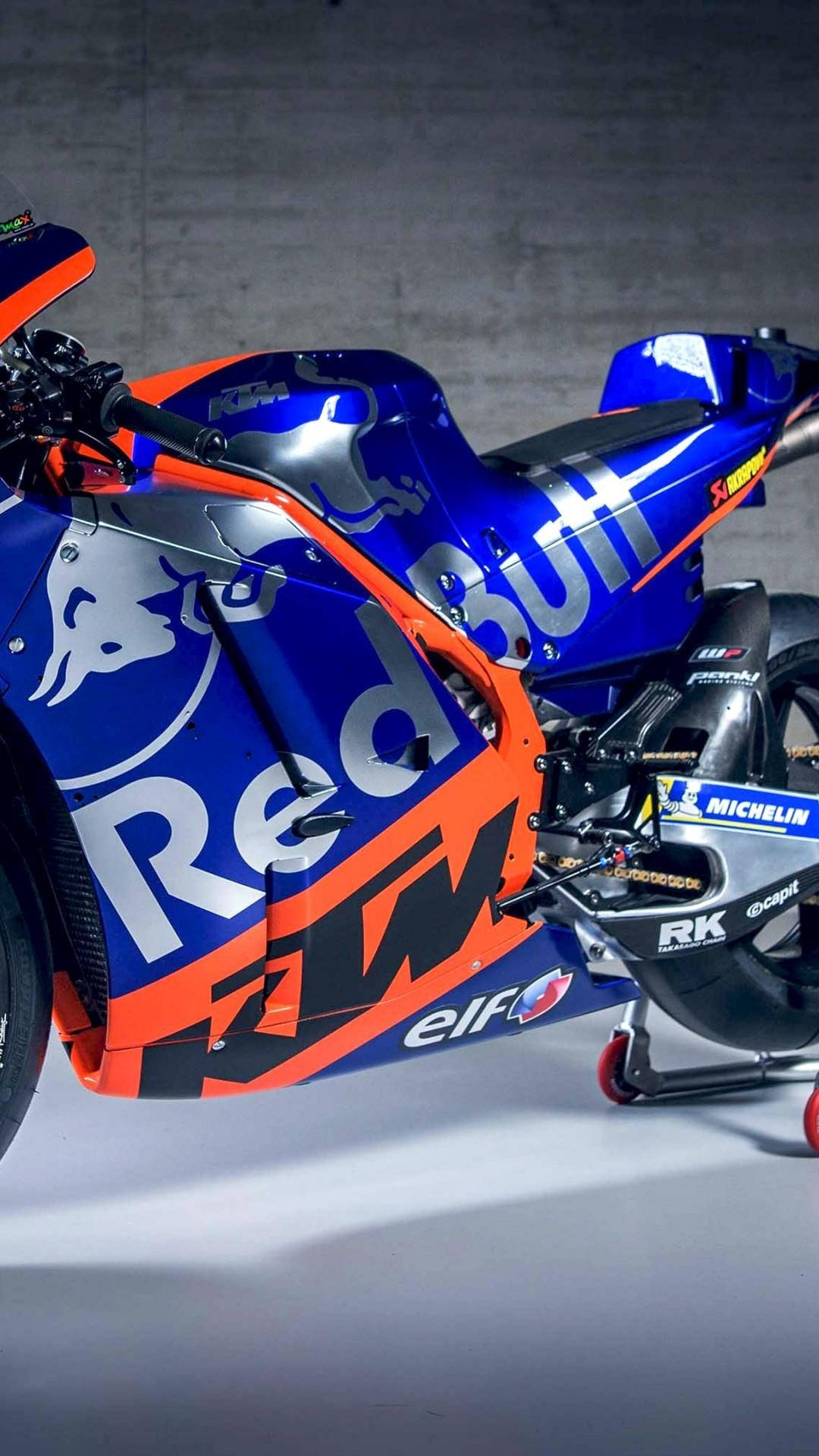 Red Bull 桌布 壁紙 — 一台時尚的藍橙色Red Bull KTM MotoGP機車，配備米其林輪胎，在混凝土牆和聚光燈的攝影棚中擺拍。