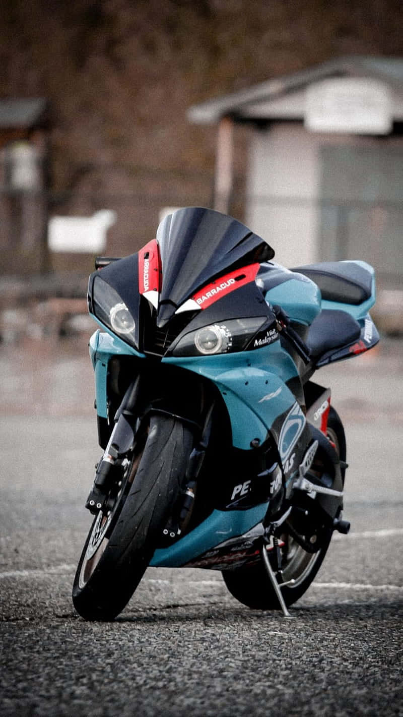 Superbike 桌布 壁紙 — 一台時尚的藍綠色和黑色運動機車停在柏油路上，背景有一座模糊的鄉村風格建築。