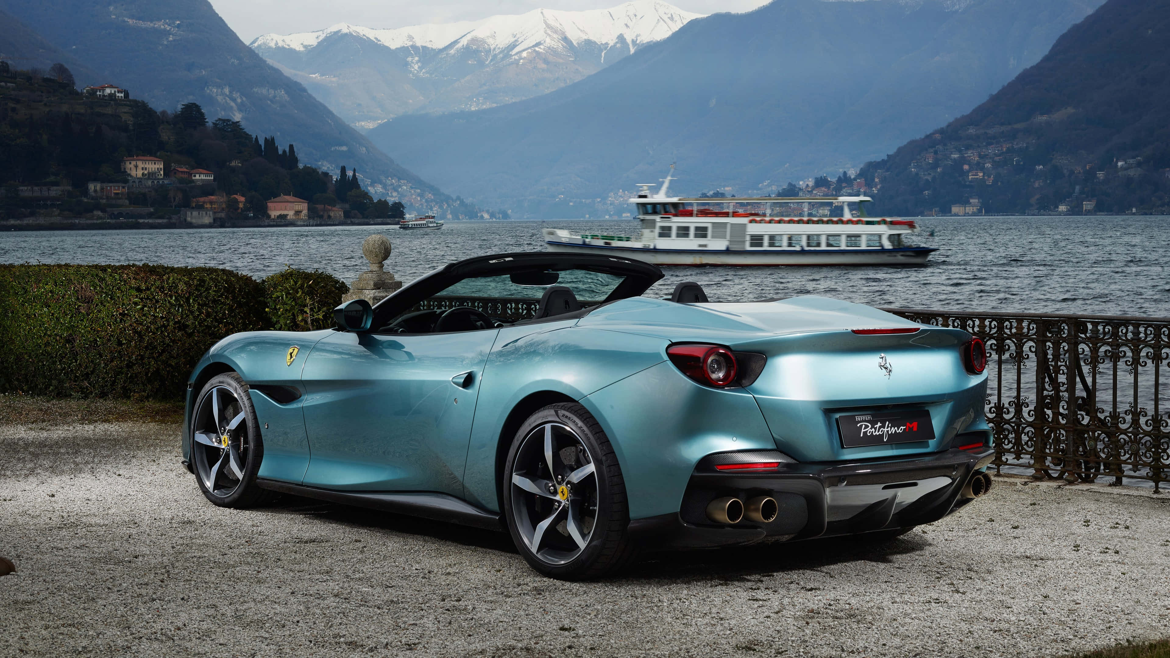 Ferrari Portofino 桌布 壁紙 — 一台時尚的藍綠色法拉利Portofino停泊在湖邊，背景是白雪皚皚的山脈和遊輪。