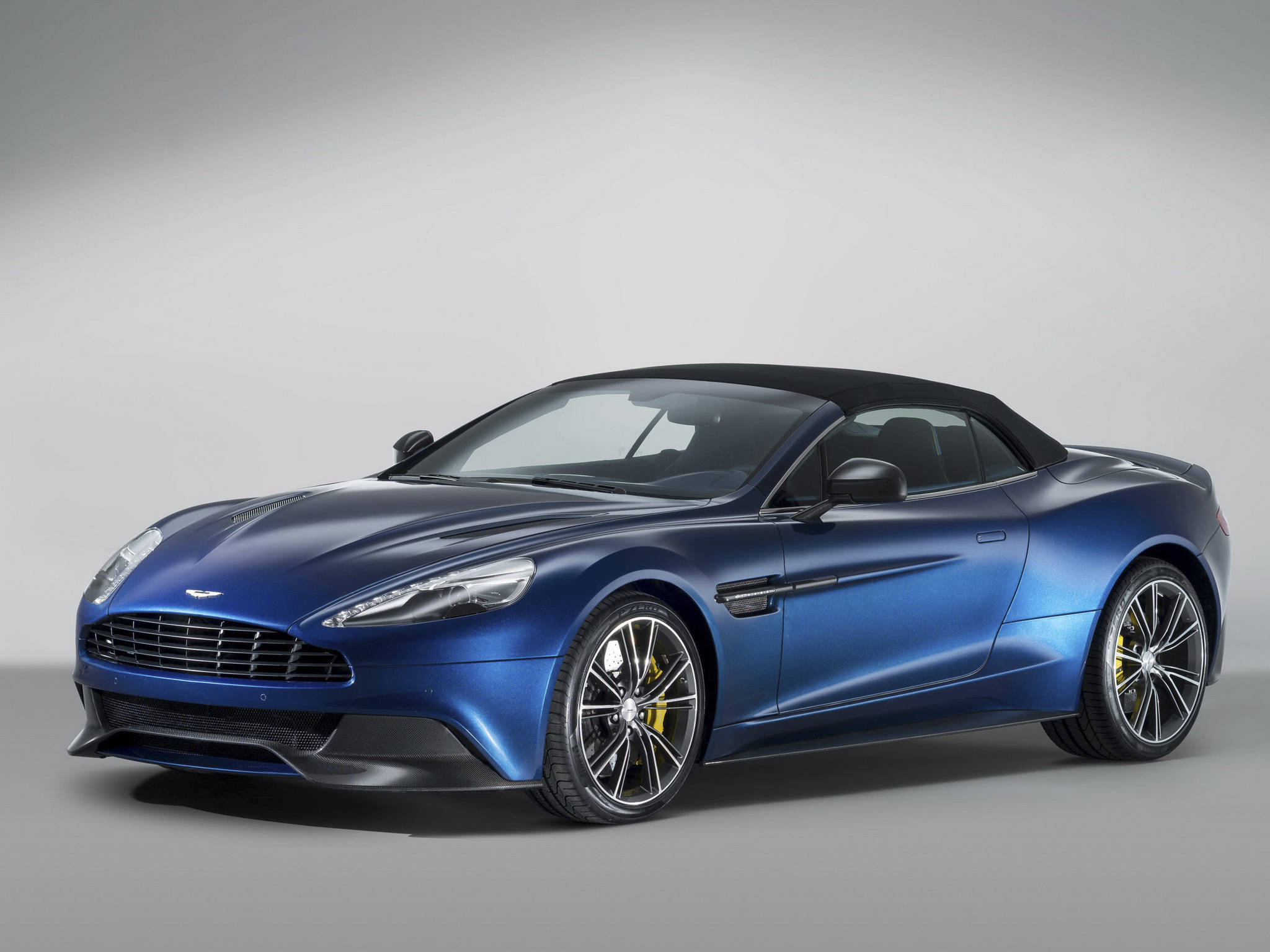 奧斯頓馬丁 桌布 壁紙 — 一台時尚的藍色 Aston Martin 敞篷車，配備黑色軟頂和黃色制動卡鉗，在灰色工作室背景前擺拍。
