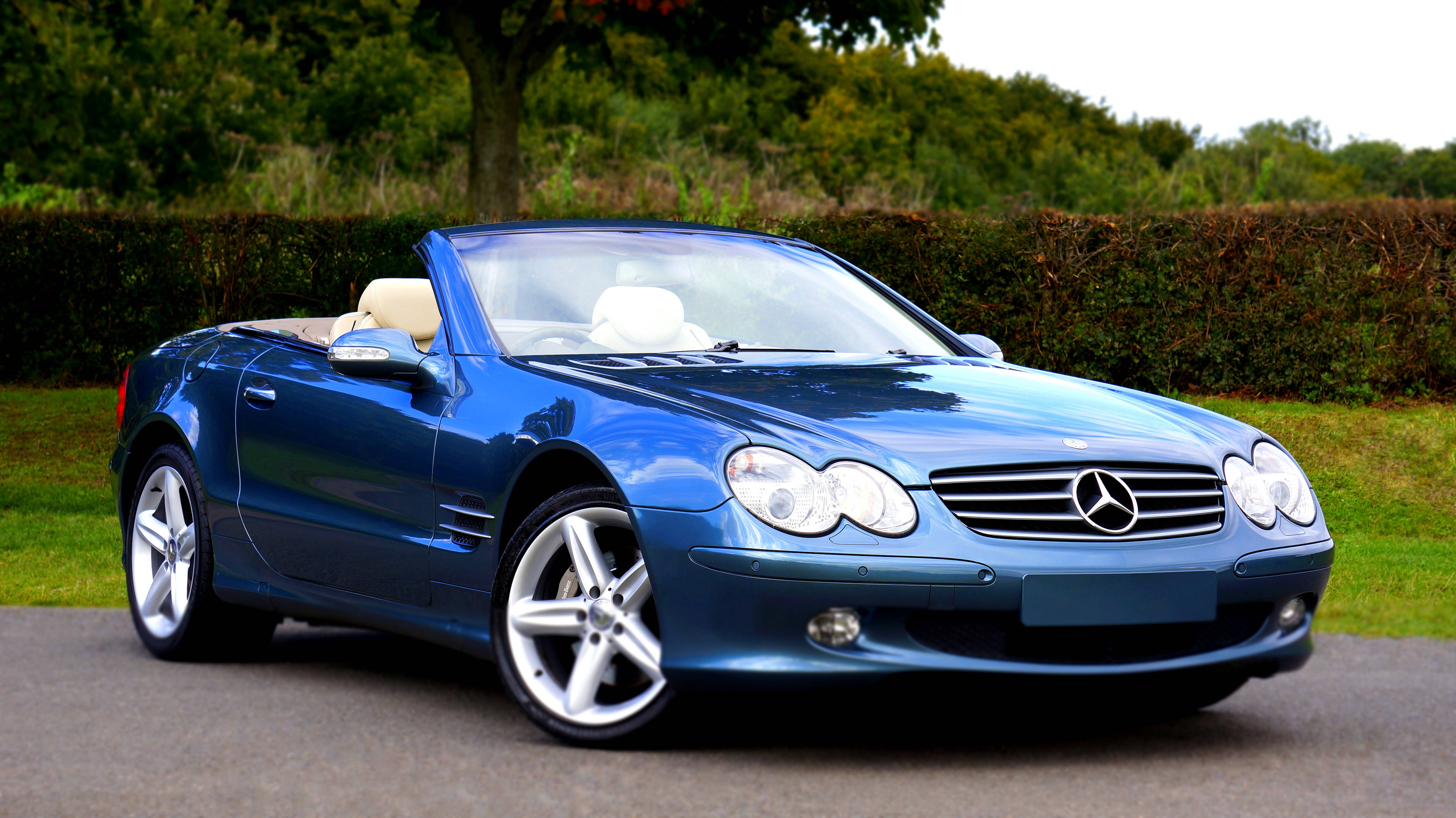 benz 4K 桌布 壁紙 — 一台時尚的藍色 Mercedes SLR McLaren 敞篷跑車停放在鋪砌的道路上，背景有綠色樹籬和樹木。