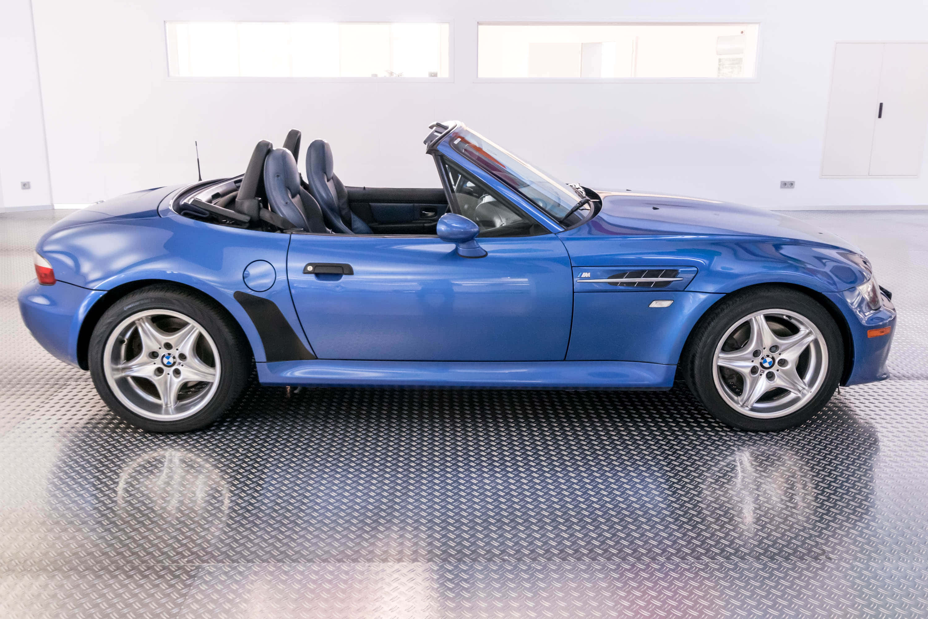 Bmw Z3 桌布 壁紙 — 一台時尚的藍色BMW Z8敞篷跑車，車頂敞開，停放在明亮白色車庫的鑽石紋地板上。