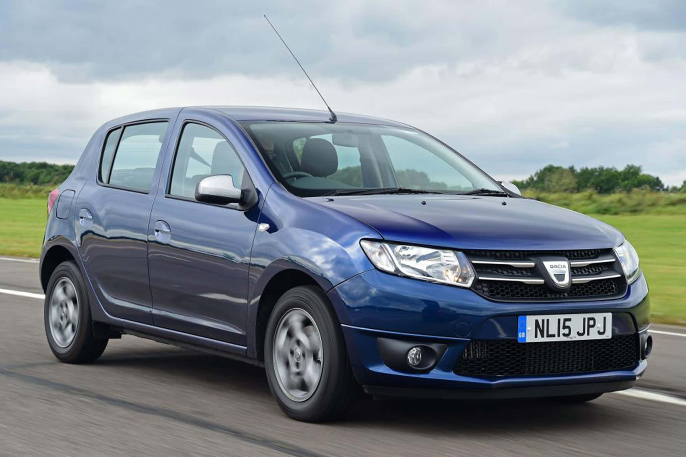 Dacia 桌布 壁紙 — 一台時尚的藍色Dacia Sandero掀背車在道路上行駛，背景是模糊的綠色田野和陰天。