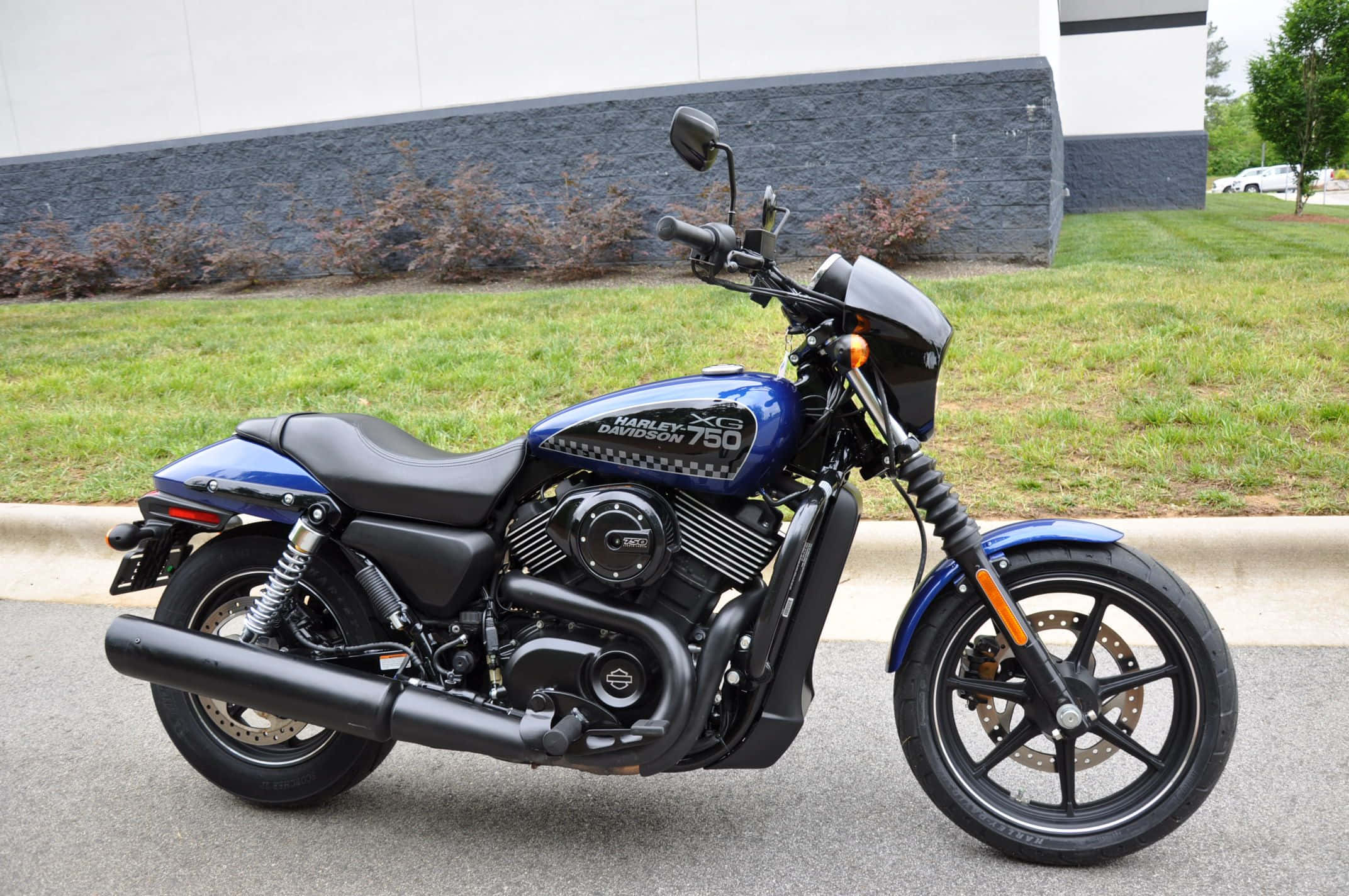 哈雷戴維森 桌布 壁紙 — 一台時尚的藍色Harley-Davidson XG 750機車停放在人行道上，旁邊有草地和現代建築。