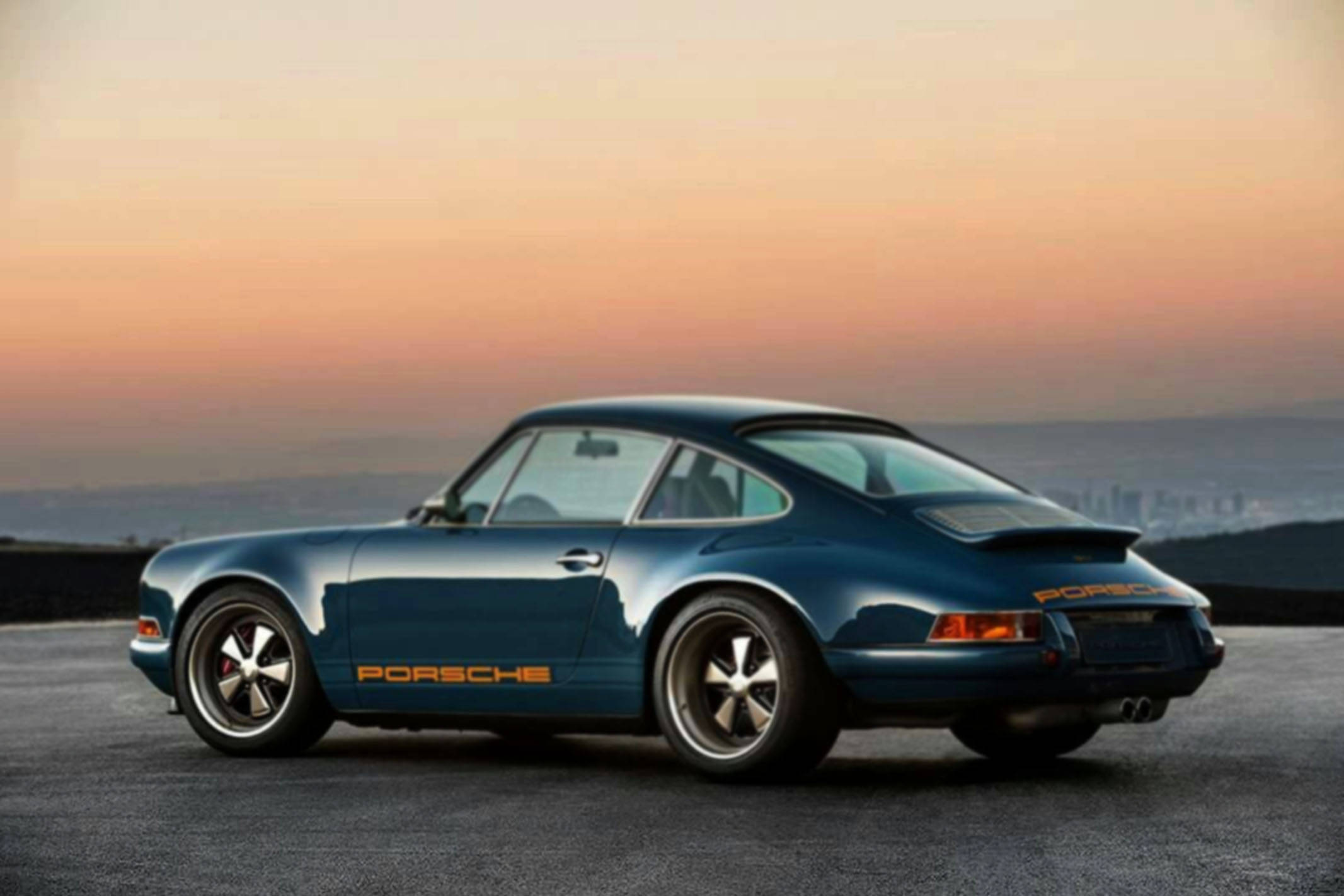 Singer 桌布 壁紙 — 一台時尚的藍色保時捷911經典跑車停泊在山頂上，夕陽西下，遠處是城市景觀。