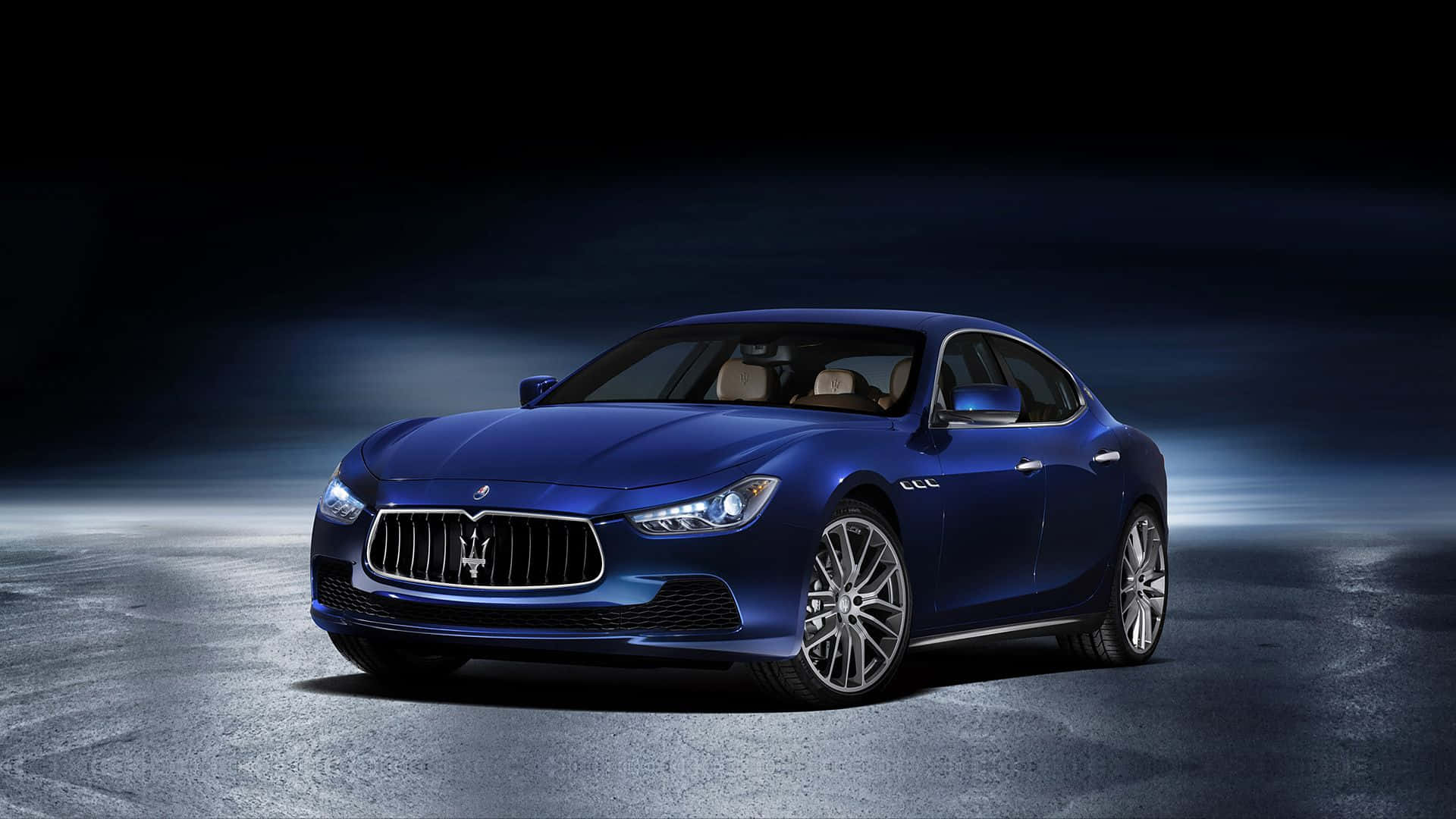 Maserati Ghibli 桌布 壁紙 — 一台時尚的藍色瑪莎拉蒂 Quattroporte 在戲劇性的工作室燈光下，在黑暗霧濛濛的背景中閃閃發光。
