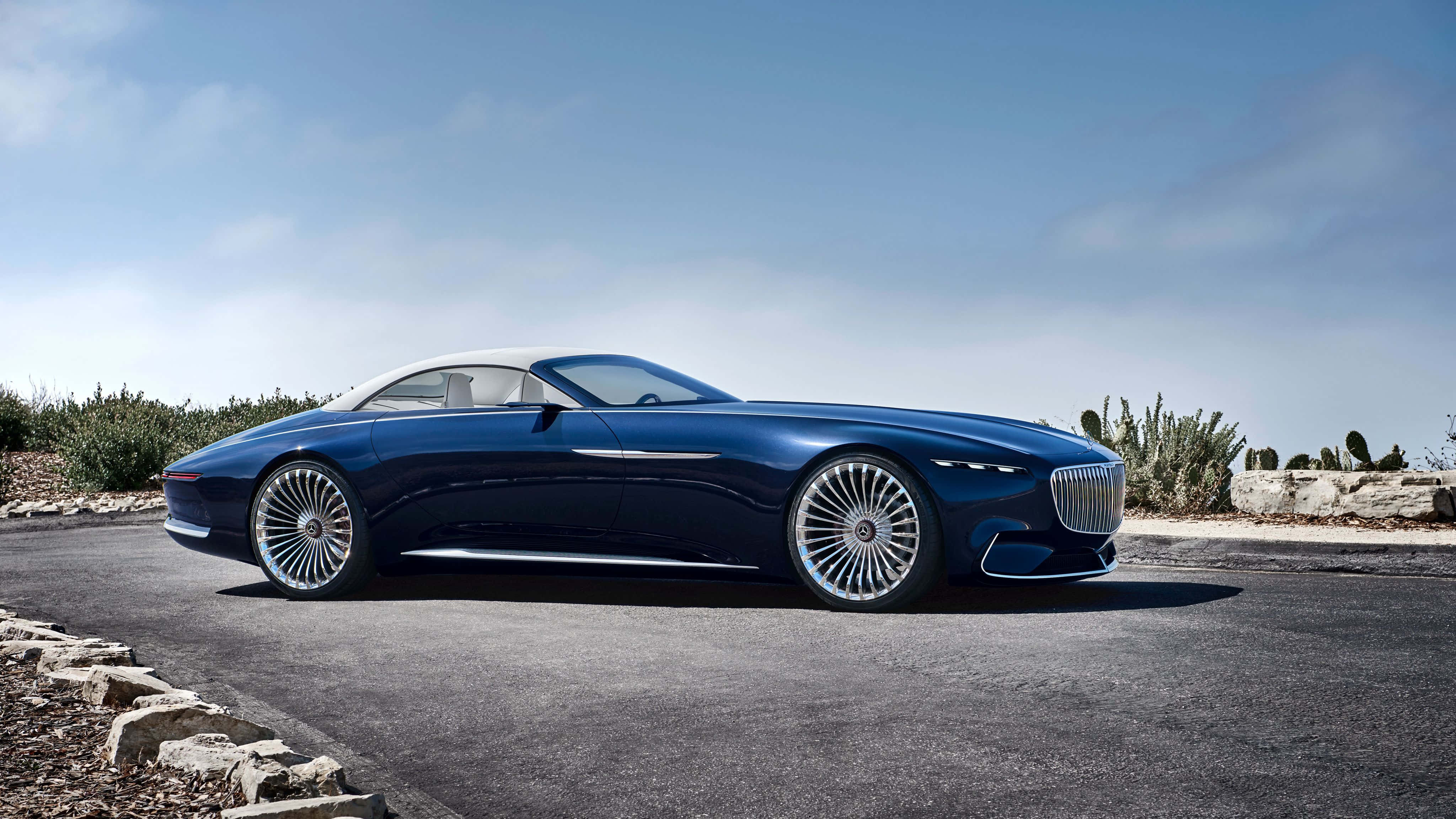 Maybach 桌布 壁紙 — 一台時尚的藍色豪華敞篷跑車，白色車頂，停在鋪砌的道路上，旁邊是沙漠仙人掌，天空清澈湛藍。