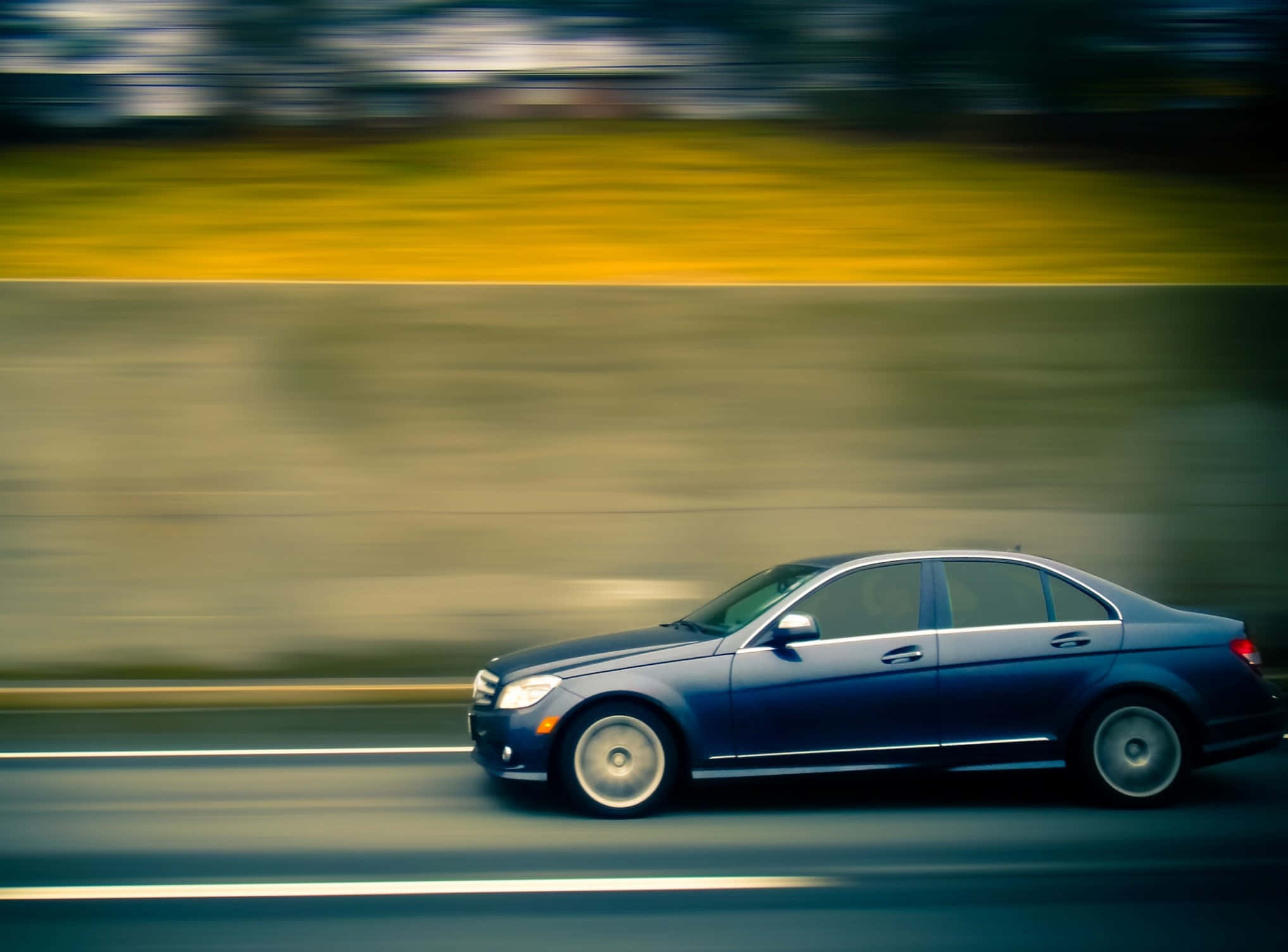 speeding car 桌布 壁紙 — 一台時尚的藍色轎車高速駛過，路邊景色在溫暖的黃色和清涼的綠色色調中變得模糊。