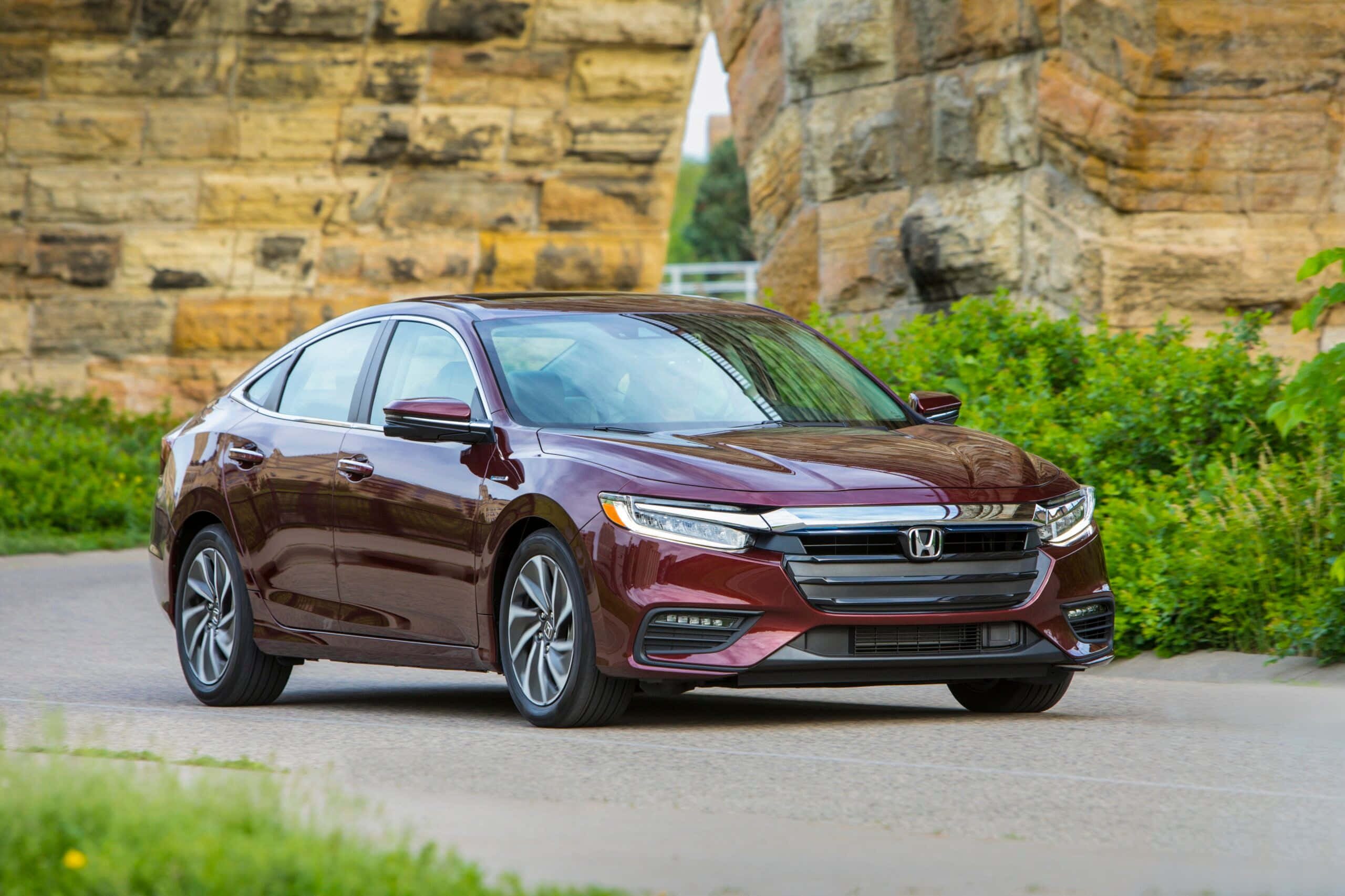 Honda Insight 桌布 壁紙 — 一台時尚的酒紅色本田轎車在明亮的日光下閃耀，停泊在石牆和綠化旁的柏油路上。