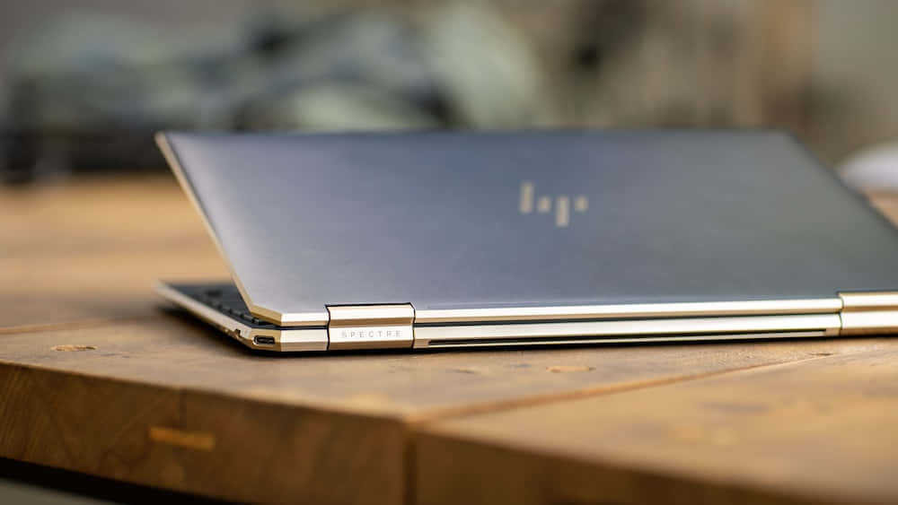 HP 桌布 壁紙 — 一台時尚的銀色 HP Spectre 筆記型電腦闔上，放在質樸的木桌上，柔和自然光線。
