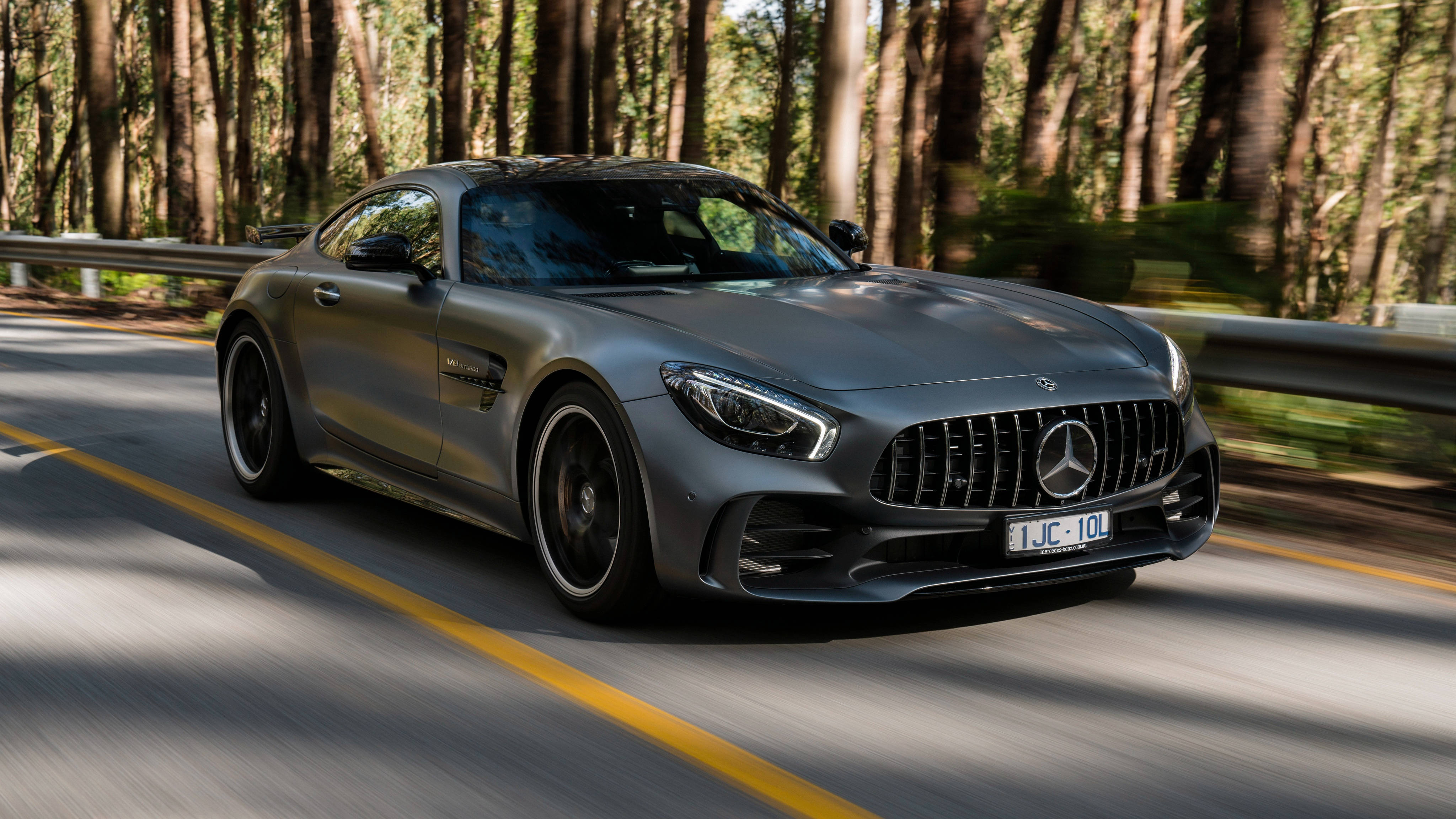 Gtr 桌布 壁紙 — 一台時尚的銀色 Mercedes-AMG GT R 在陽光明媚的森林道路上奔馳，車輪和樹木呈現動態模糊效果。