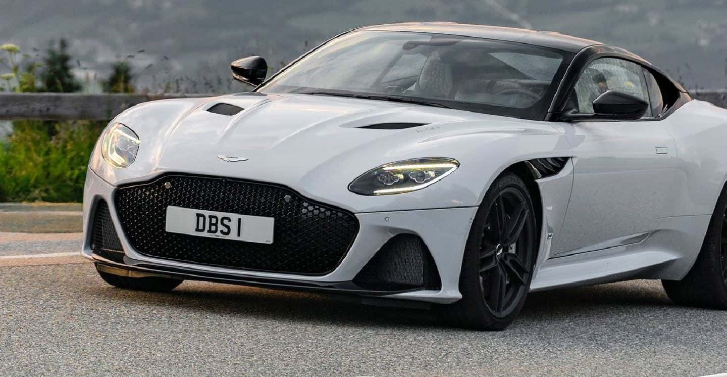 Aston Martin Dbs Superleggera 桌布 壁紙 — 一台時尚的銀色Aston Martin DBS1跑車停在蜿蜒的山路上，背景是翠綠的山丘。