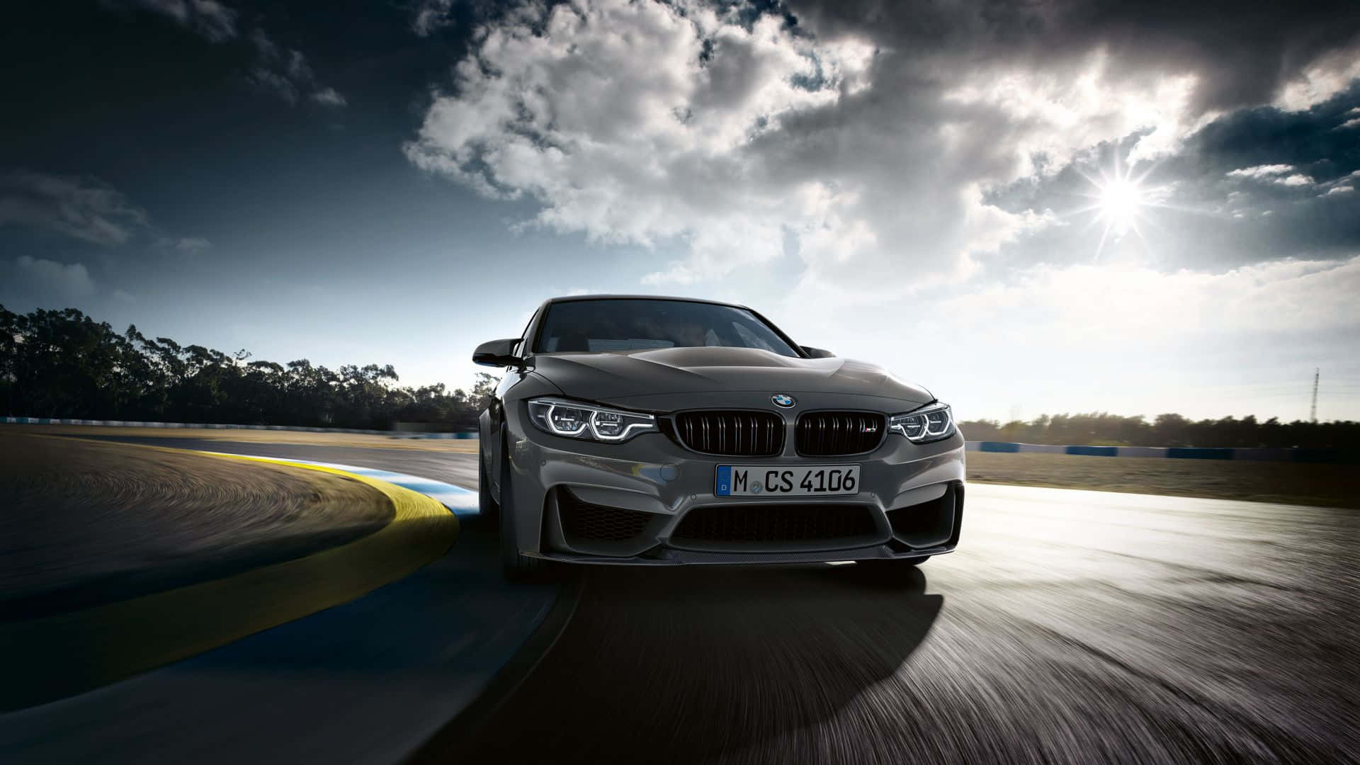 Cloudy Sky 桌布 壁紙 — 一台時尚的銀色BMW M4 CS在潮濕的賽道上奔馳，天空戲劇性地陽光普照並伴有暴風雲。