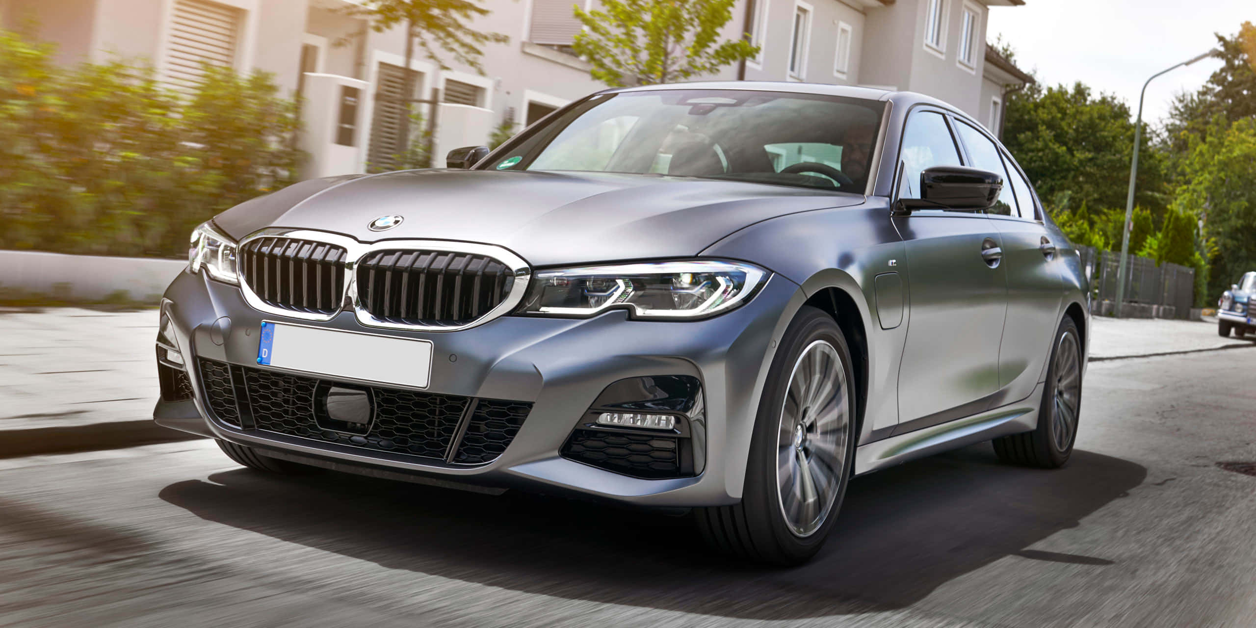 Bmw 3 Series 桌布 壁紙 — 一台時尚的銀色寶馬轎車在陽光明媚的住宅街道上滑行，動態模糊強調速度。