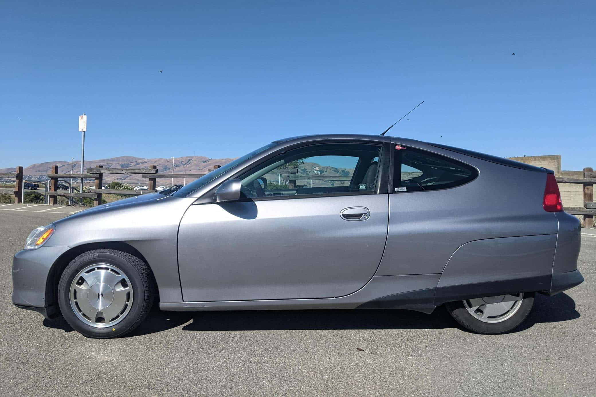Honda Insight 桌布 壁紙 — 一台時尚的銀色本田Insight混合動力雙門轎跑車停放在陽光明媚的停車場，遠方有山丘，天空清澈湛藍。