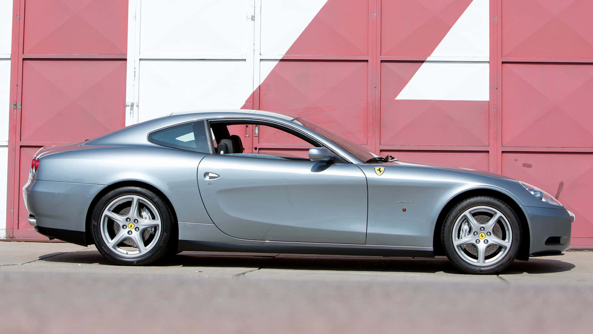 Ferrari 612 Scaglietti 桌布 壁紙 — 一台時尚的銀色法拉利612 Superamerica雙門跑車停放在大膽的紅白幾何車庫門前。
