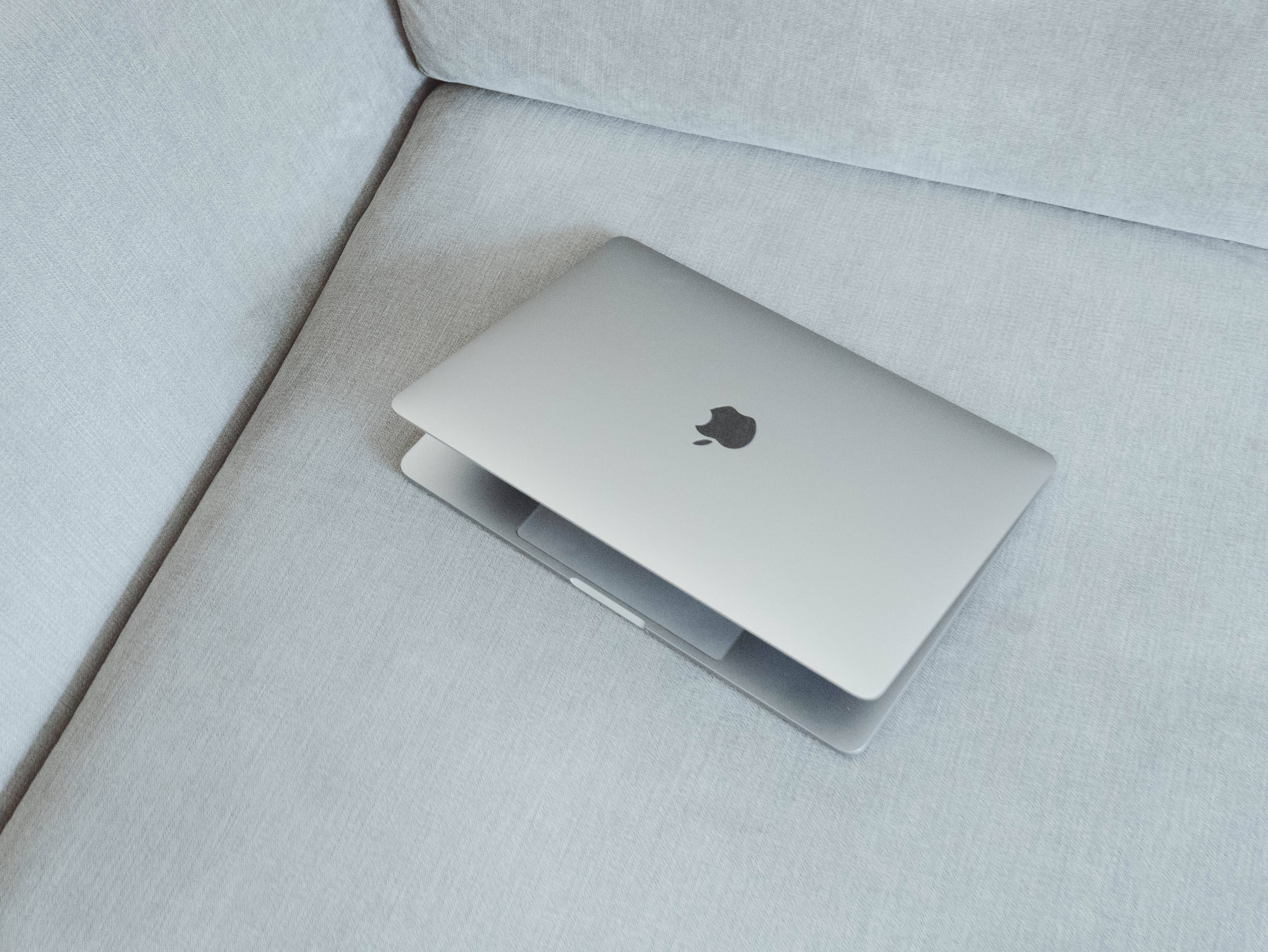 macbook pro 桌布 壁紙 — 一台時尚的銀色筆記型電腦在柔和自然光下，闔上放在淺灰色紋理沙發角落。