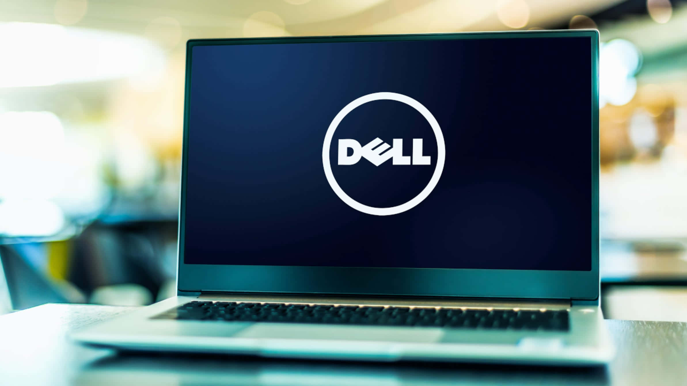 Dell 桌布 壁紙 — 一台時尚的銀色筆記型電腦在深色螢幕上顯示白色Dell標誌，背景是柔和模糊的辦公室。