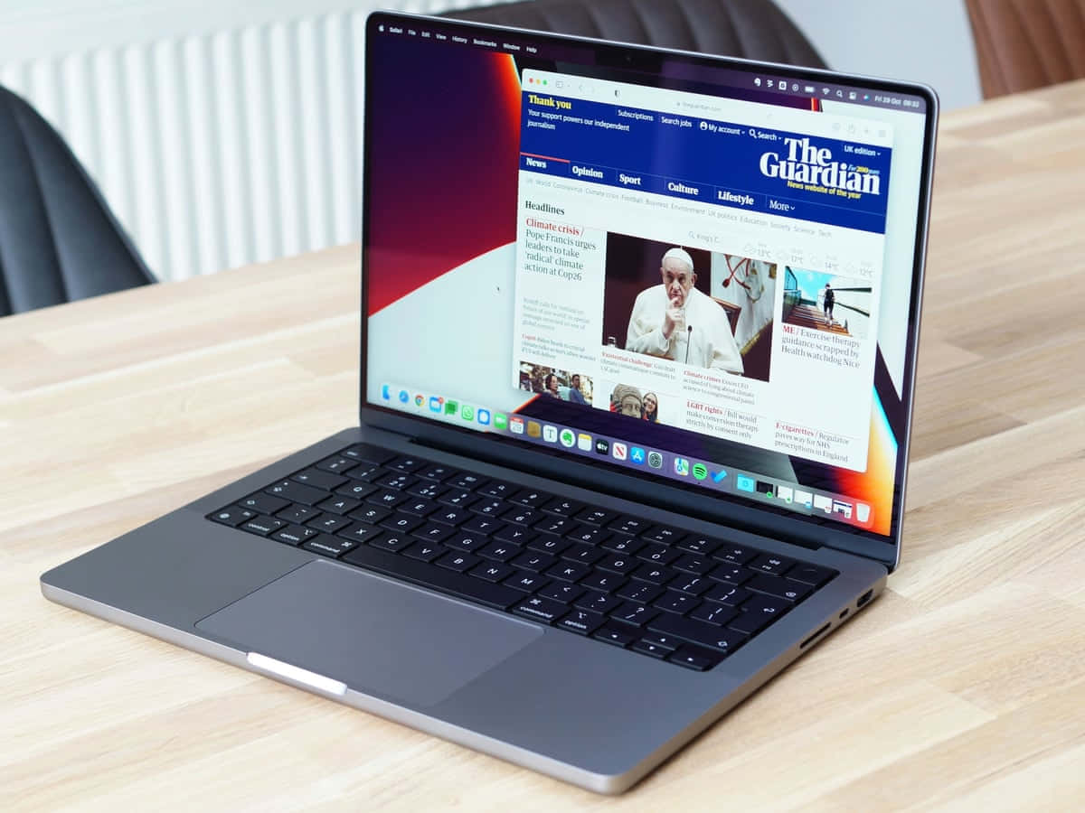 MacBook 動態圖片 桌布 壁紙 — 一台時尚的銀色筆記型電腦在現代室內環境中的木桌上顯示The Guardian新聞網站。