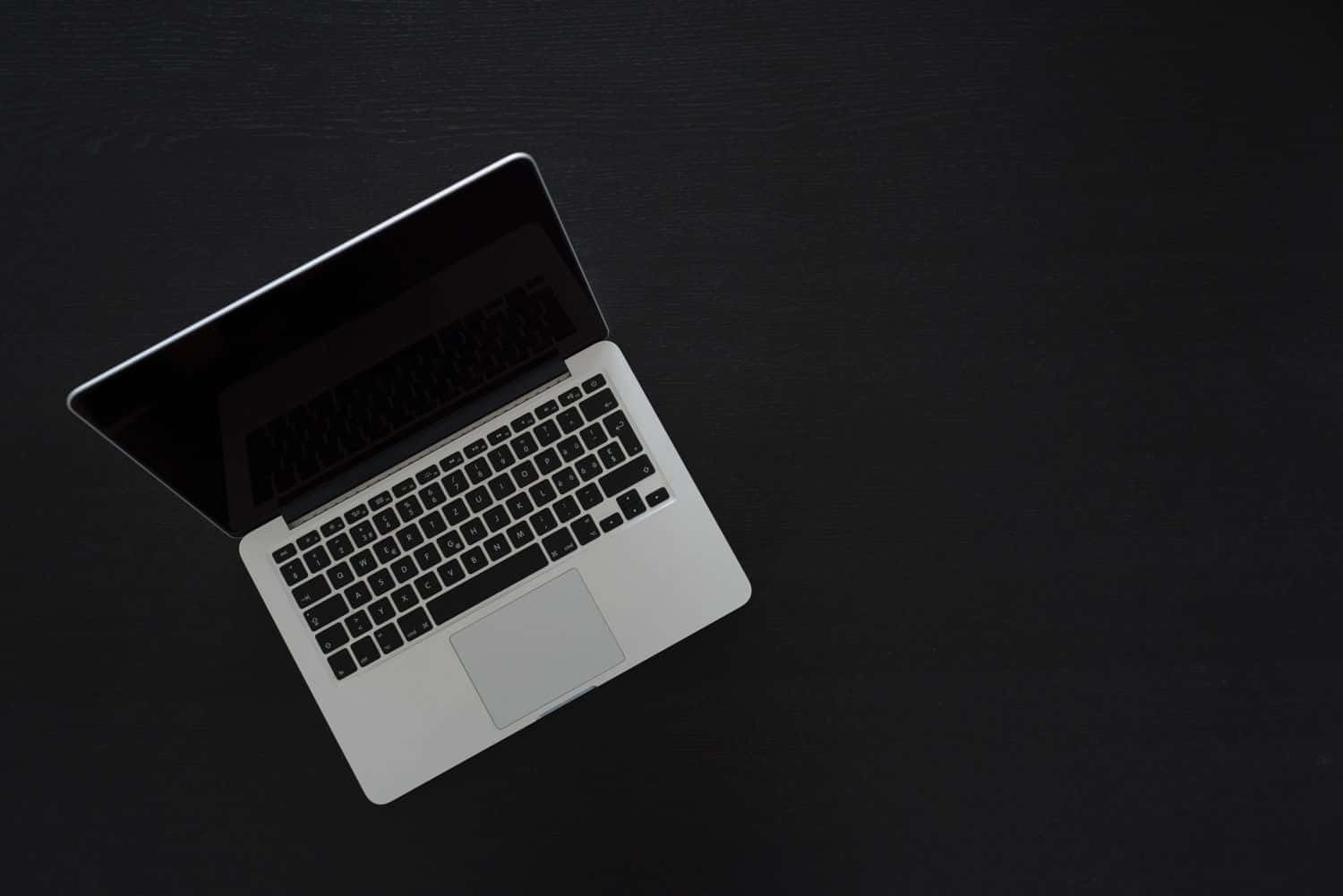 Black Macbook 桌布 壁紙 — 一台時尚的銀色筆記型電腦打開放在霧面黑色表面上，從上方觀看。