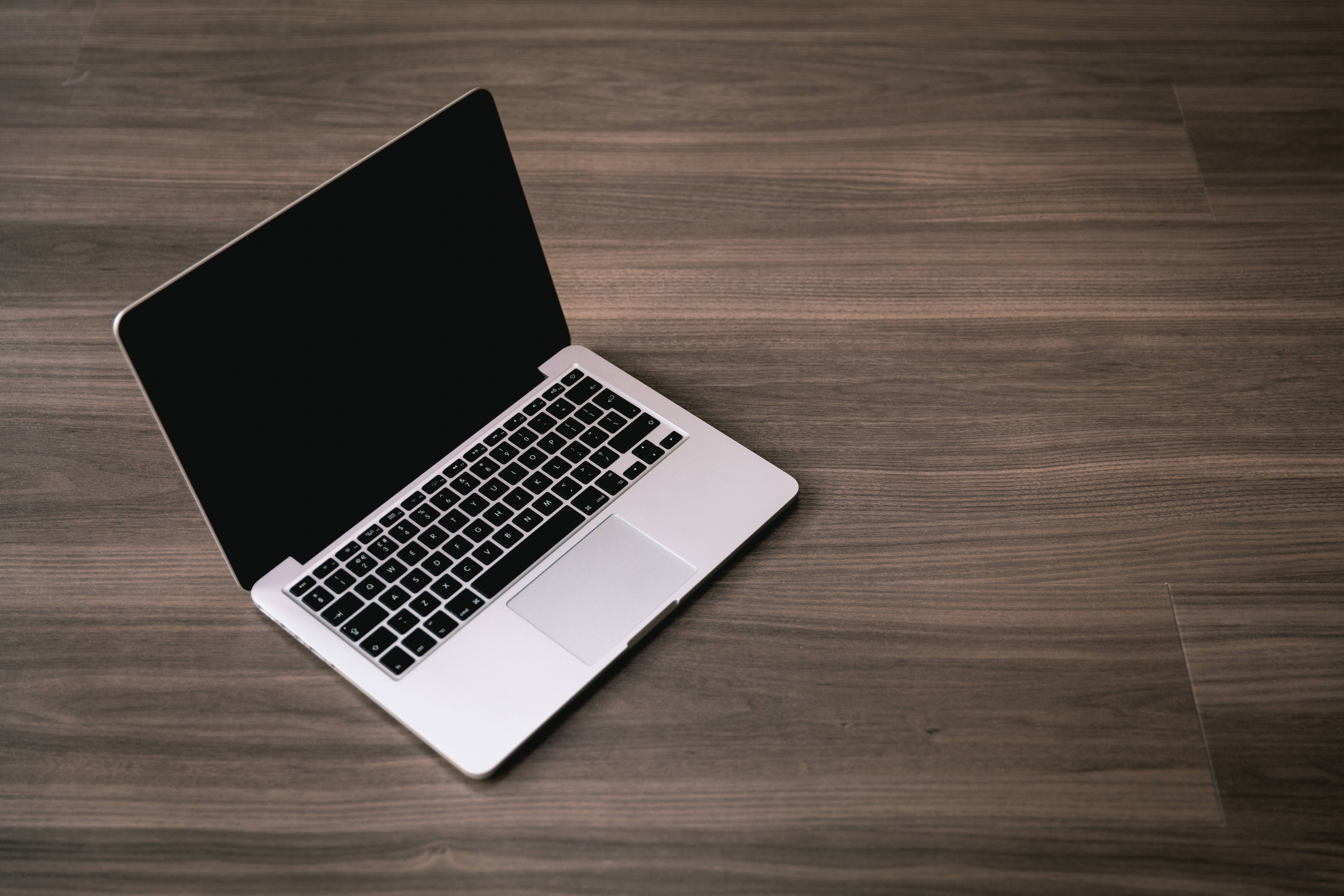 Cute Laptop 桌布 壁紙 — 一台時尚的銀色筆記型電腦打開放在深色木紋表面上，螢幕為空白黑色。