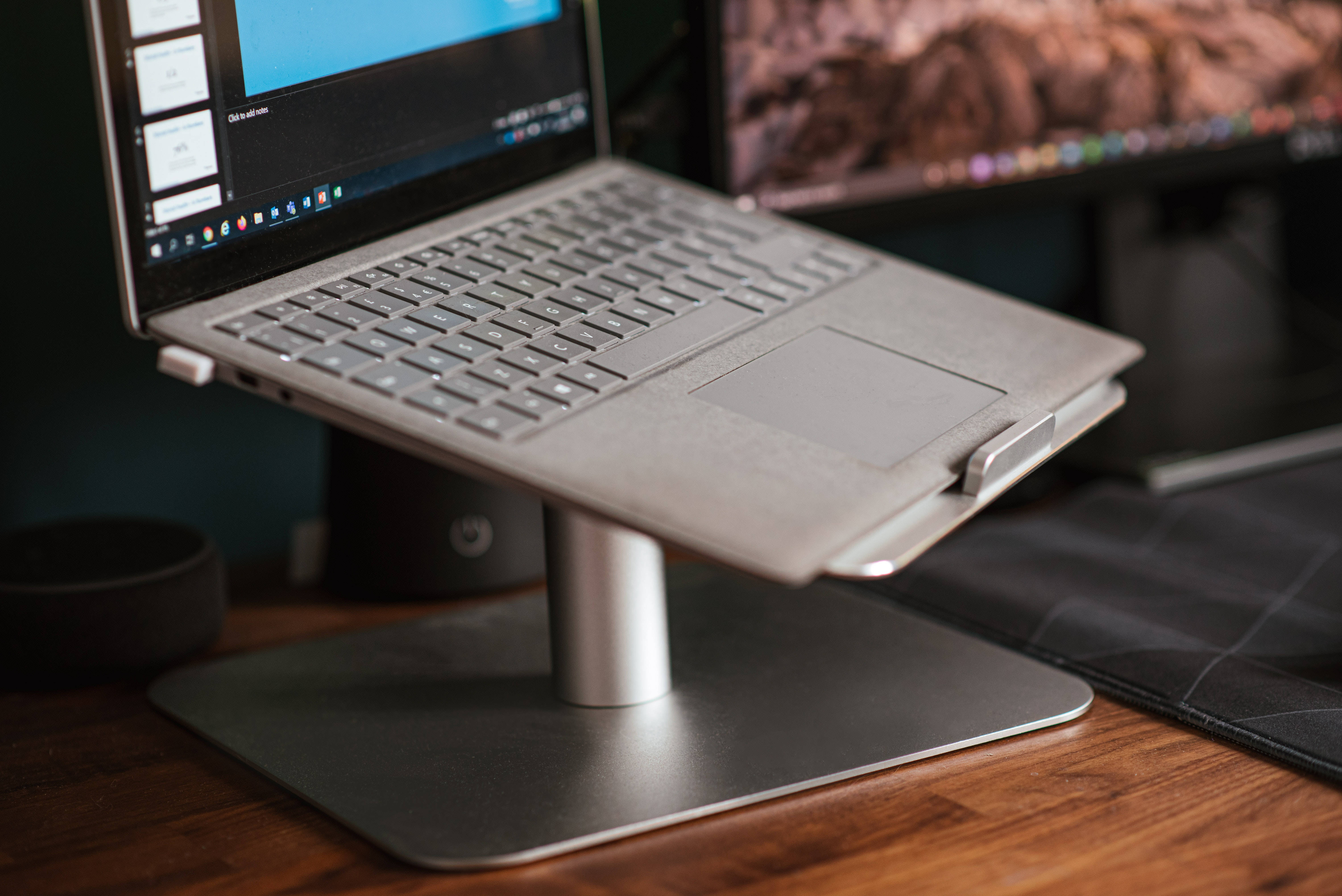 Cute Laptop 桌布 壁紙 — 一台時尚的銀色筆記型電腦放在現代支架上，旁邊是顯示山景桌布的顯示器，置於木桌上。