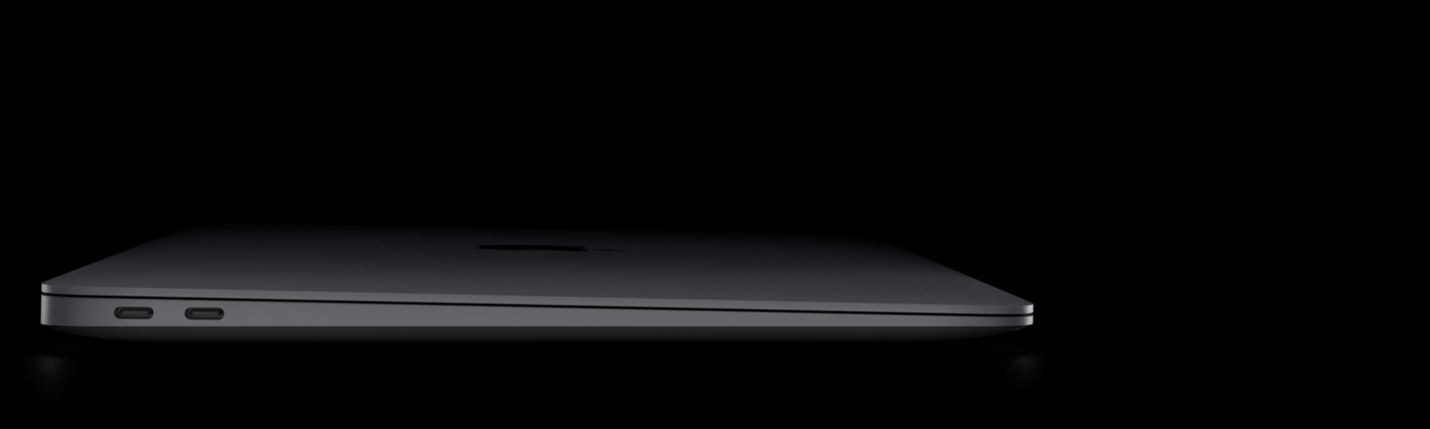 Black Macbook 桌布 壁紙 — 一台時尚的銀色筆記型電腦水平放置在純黑色背景上，柔和的光線突顯其纖薄的輪廓。