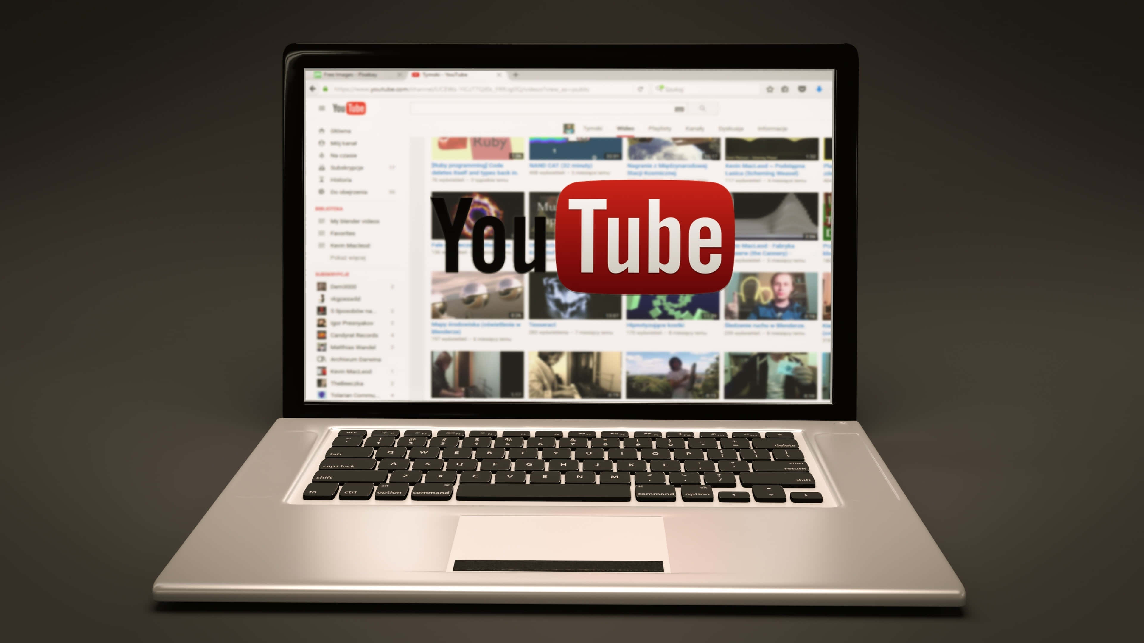 YouTube 桌布 壁紙 — 一台時尚的銀色筆記型電腦顯示YouTube首頁，在深色漸層背景上，影片縮圖中央有一個醒目的紅色標誌。